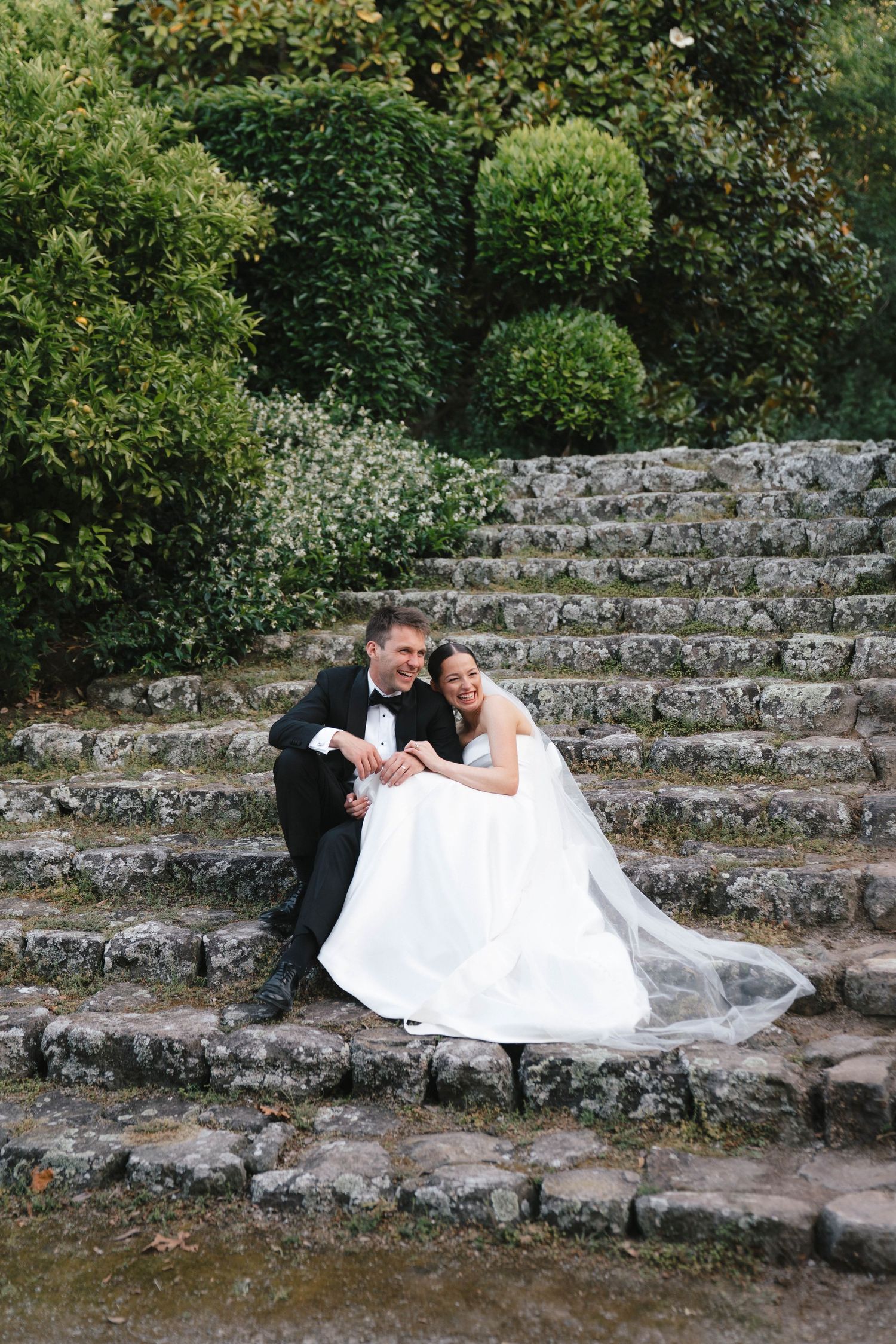 Newlyweds relaxing together on rustic stone steps surrounded by greenery.