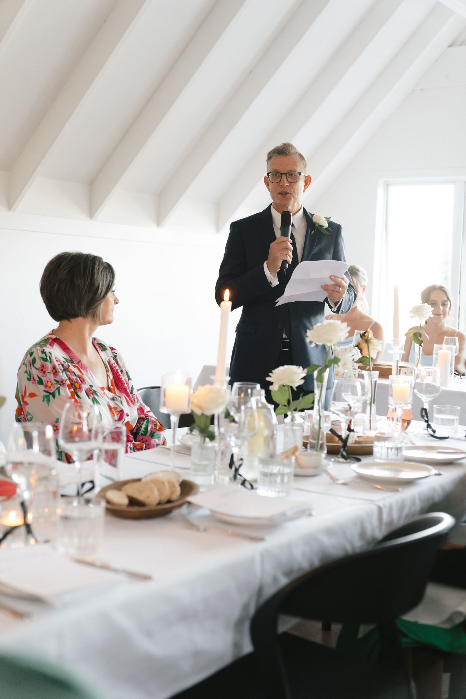 Speaker delivering toast at elegant wedding reception table in bright white room.
