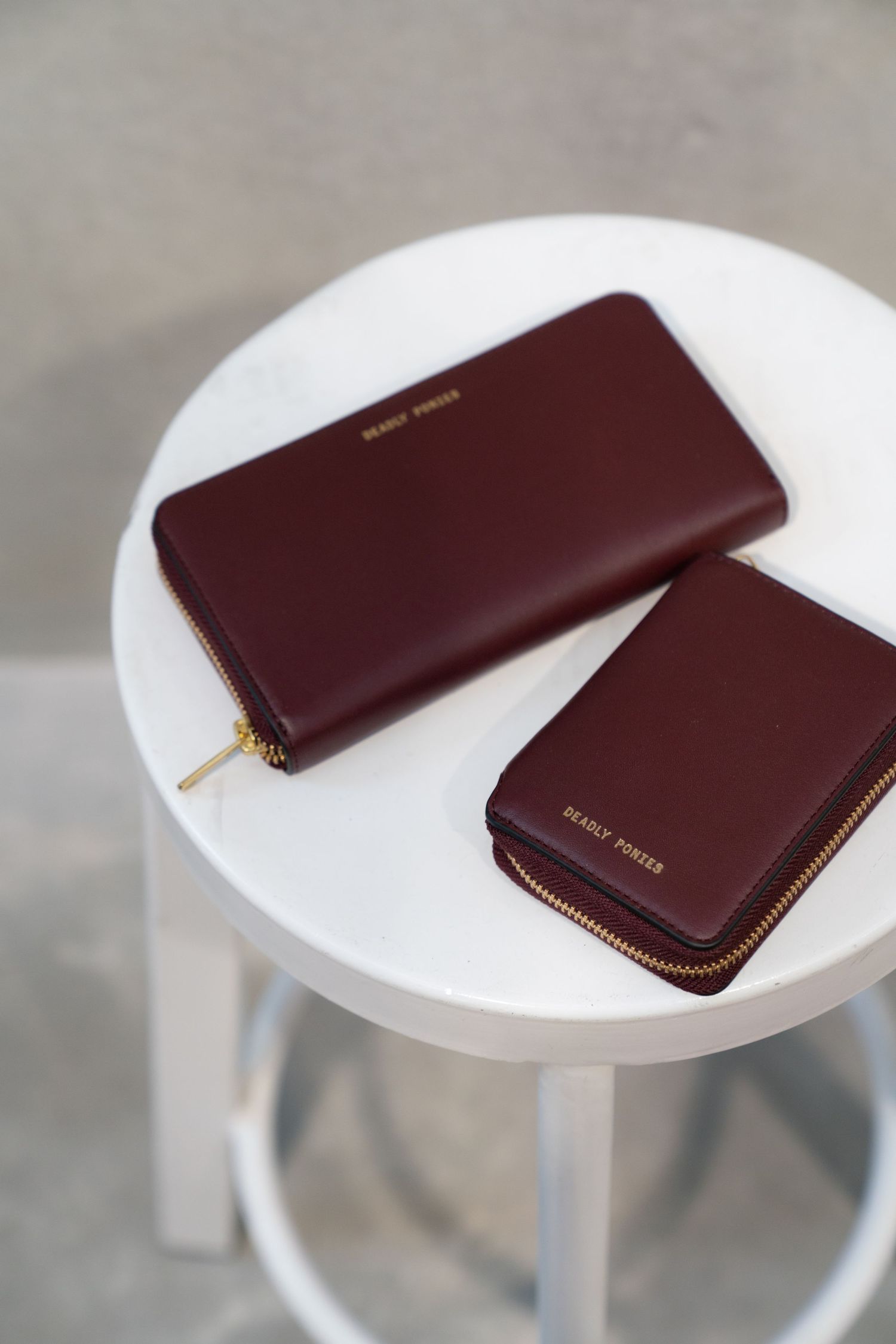 Two brown leather wallets displayed on a white round side table against a gray background.