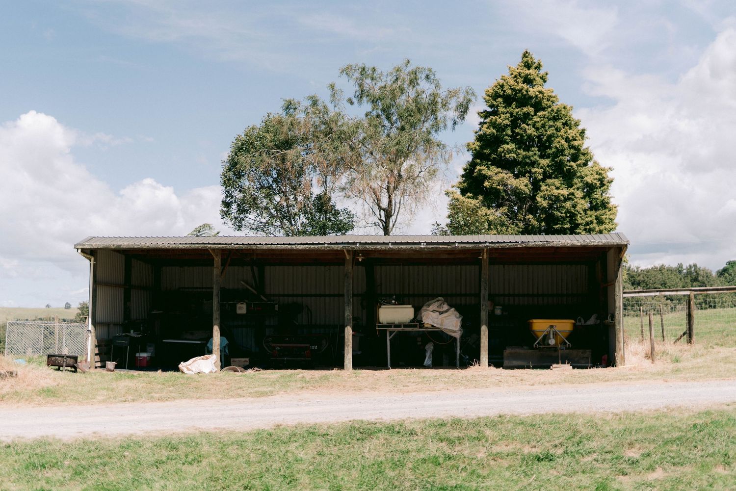 Rustic wooden barn structure with animals seeking shelter in the shade on a sunny day.