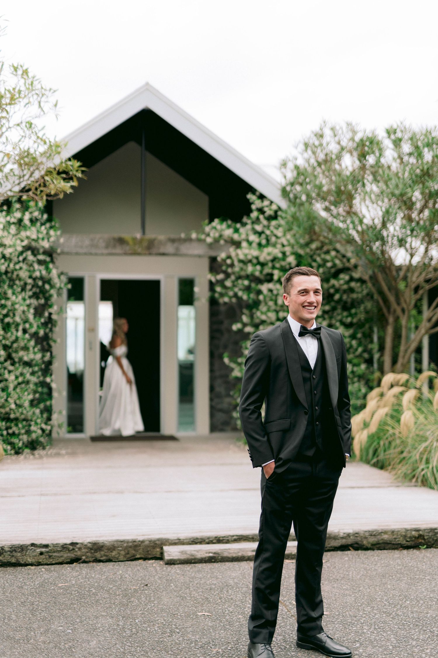 Wedding scene with person in tuxedo standing on pathway near chapel entrance.