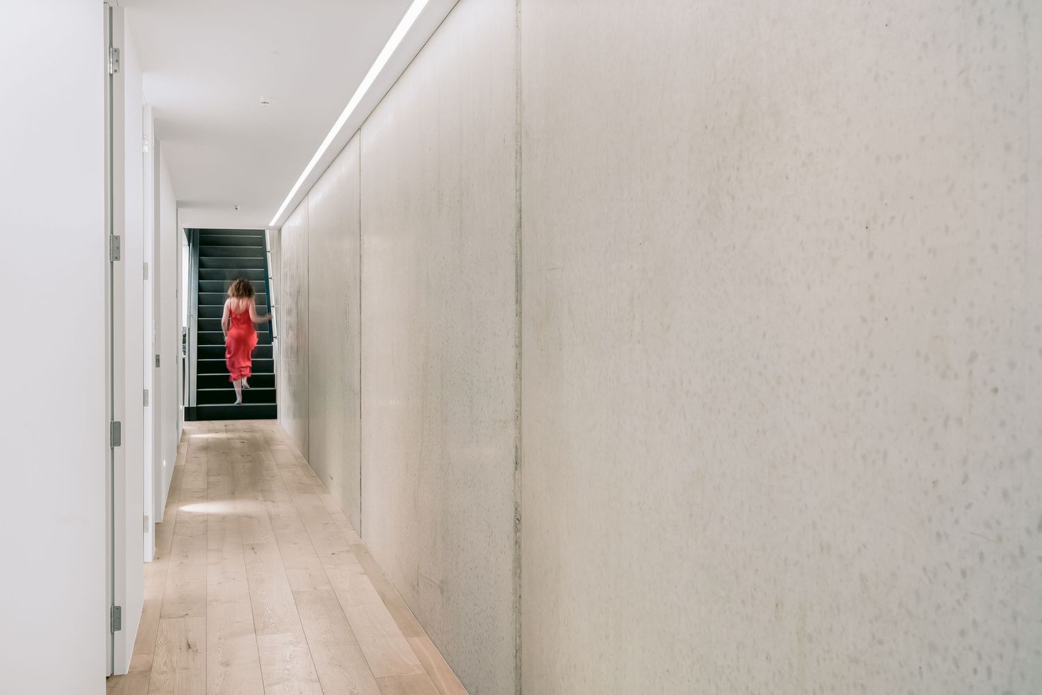 Long narrow hallway with white walls and tiled floor leading to a distant view of stairs illuminated in red light.