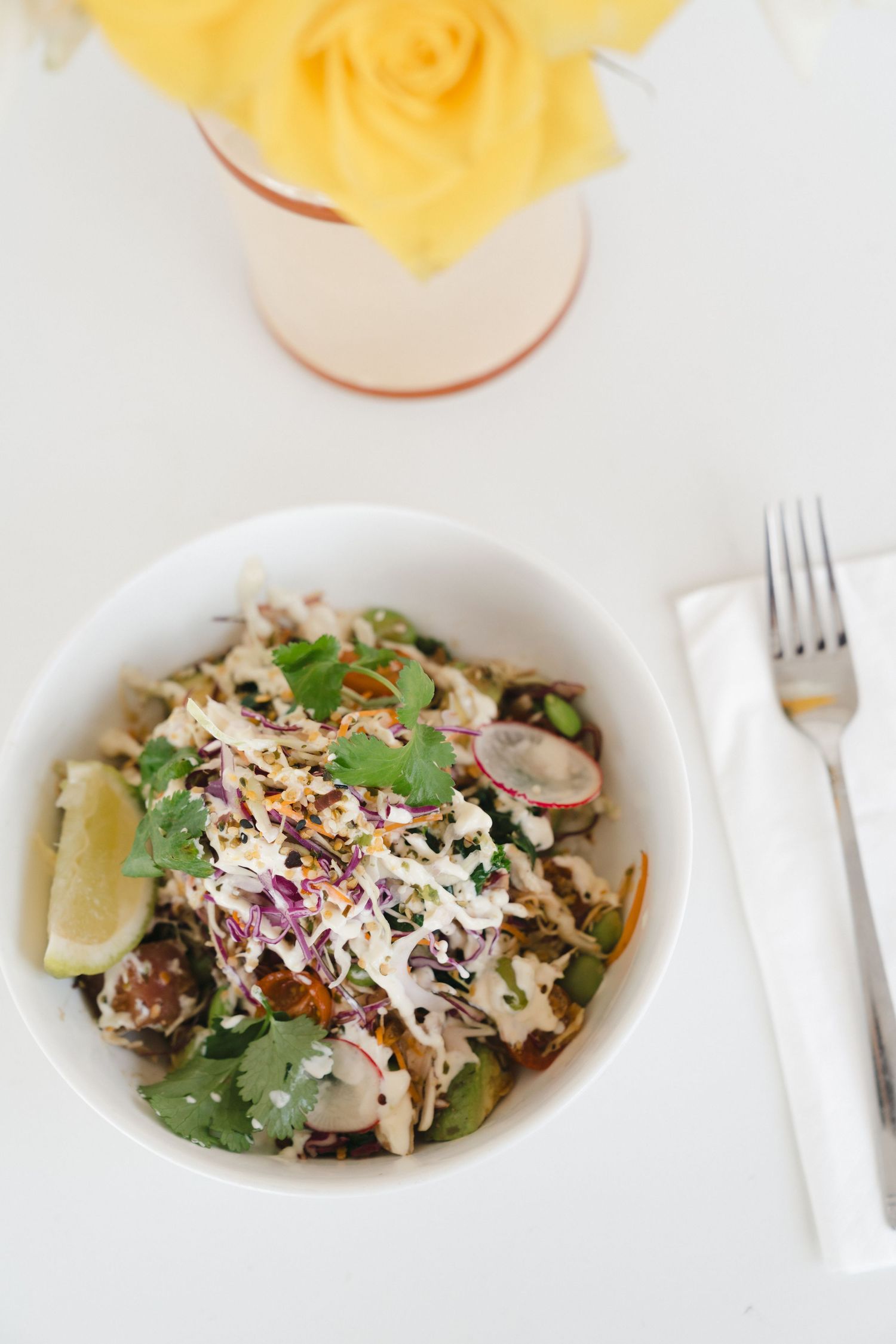 Fresh salad with shredded parmesan cheese, radishes, and greens served in a white bowl with wine glass in background.