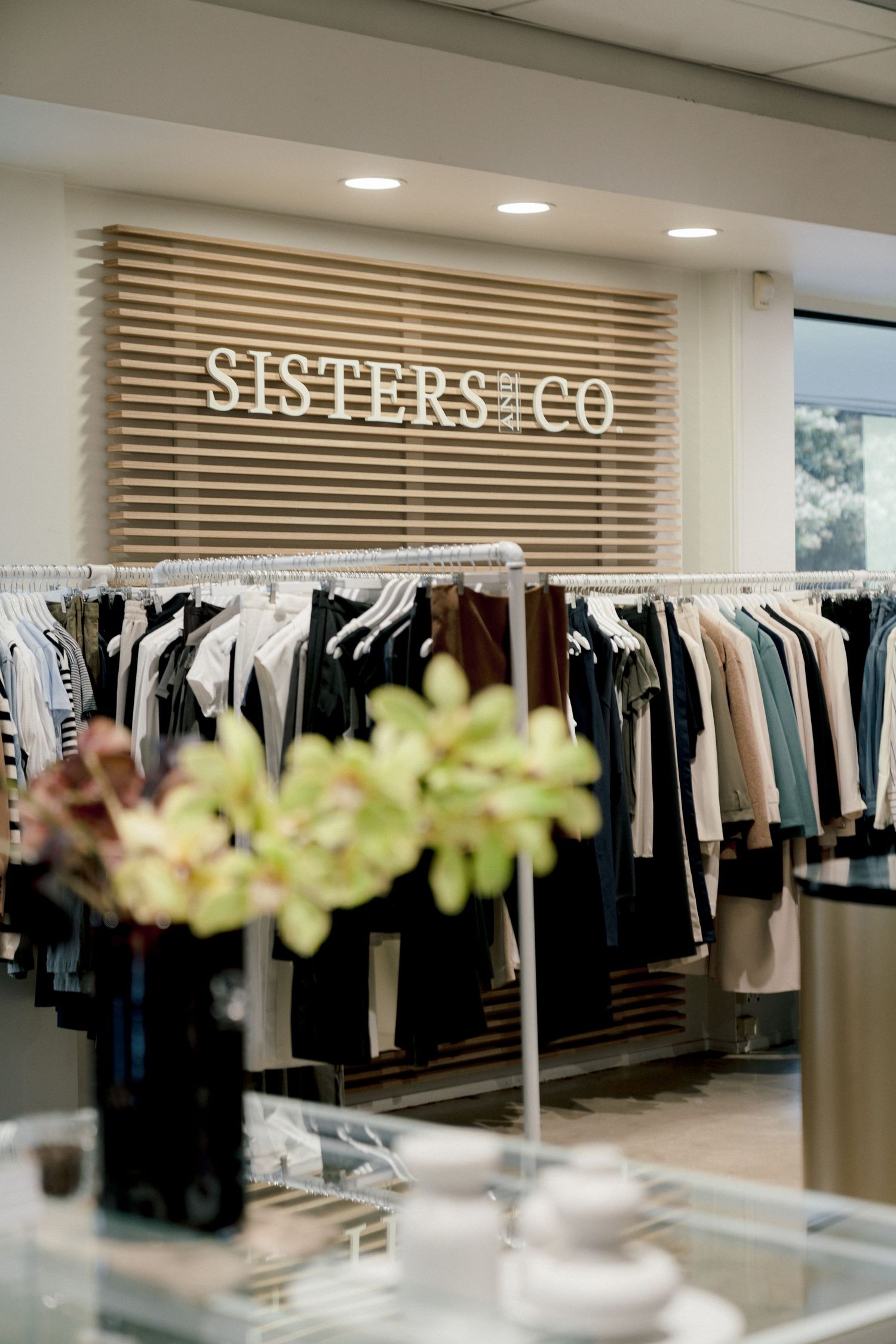 Clothing store interior displaying racks of clothing with Sisters & Co signage and modern lighting fixtures.