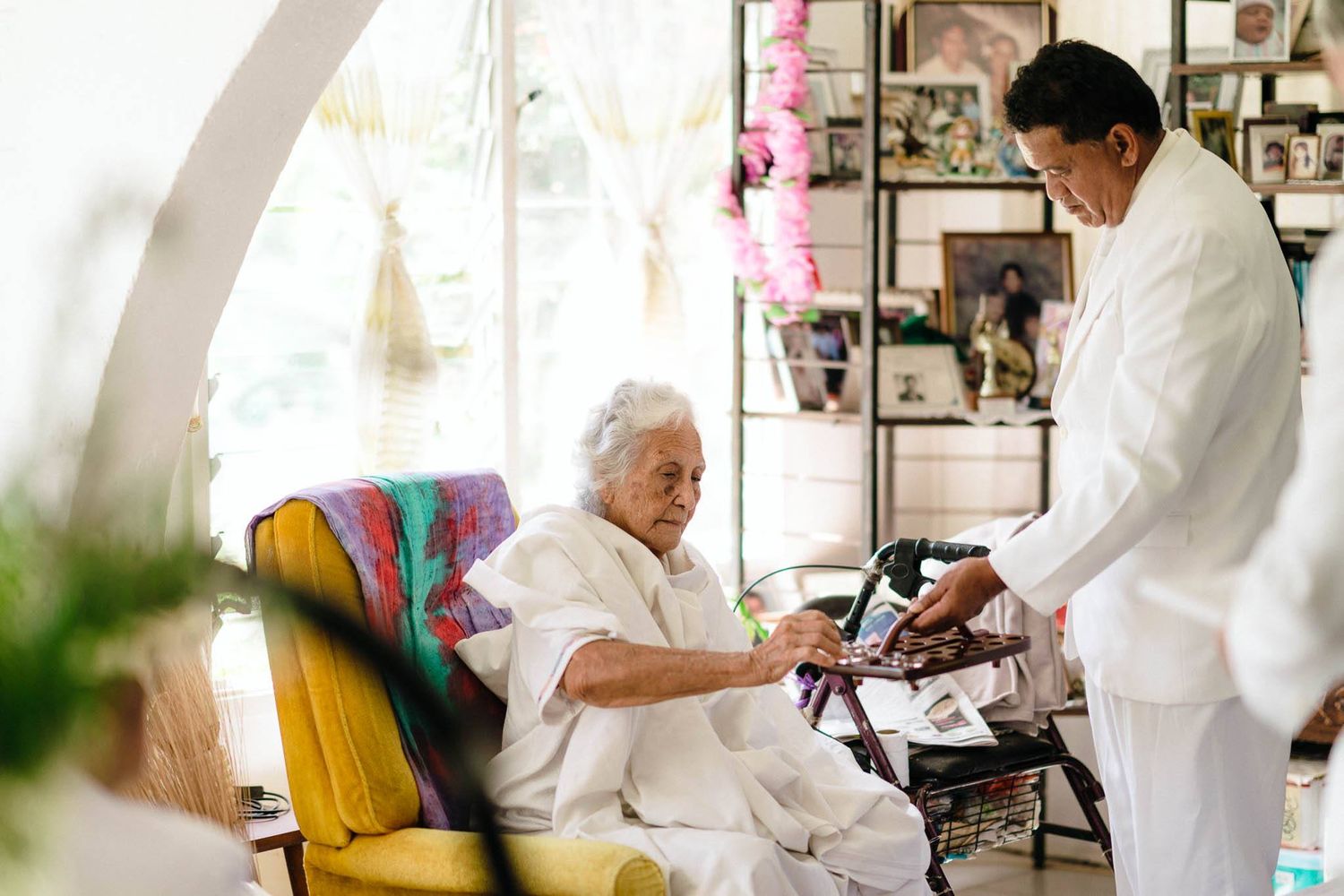 Medical professional conducting a blood pressure check on an elderly patient seated in a colorful armchair at home.
