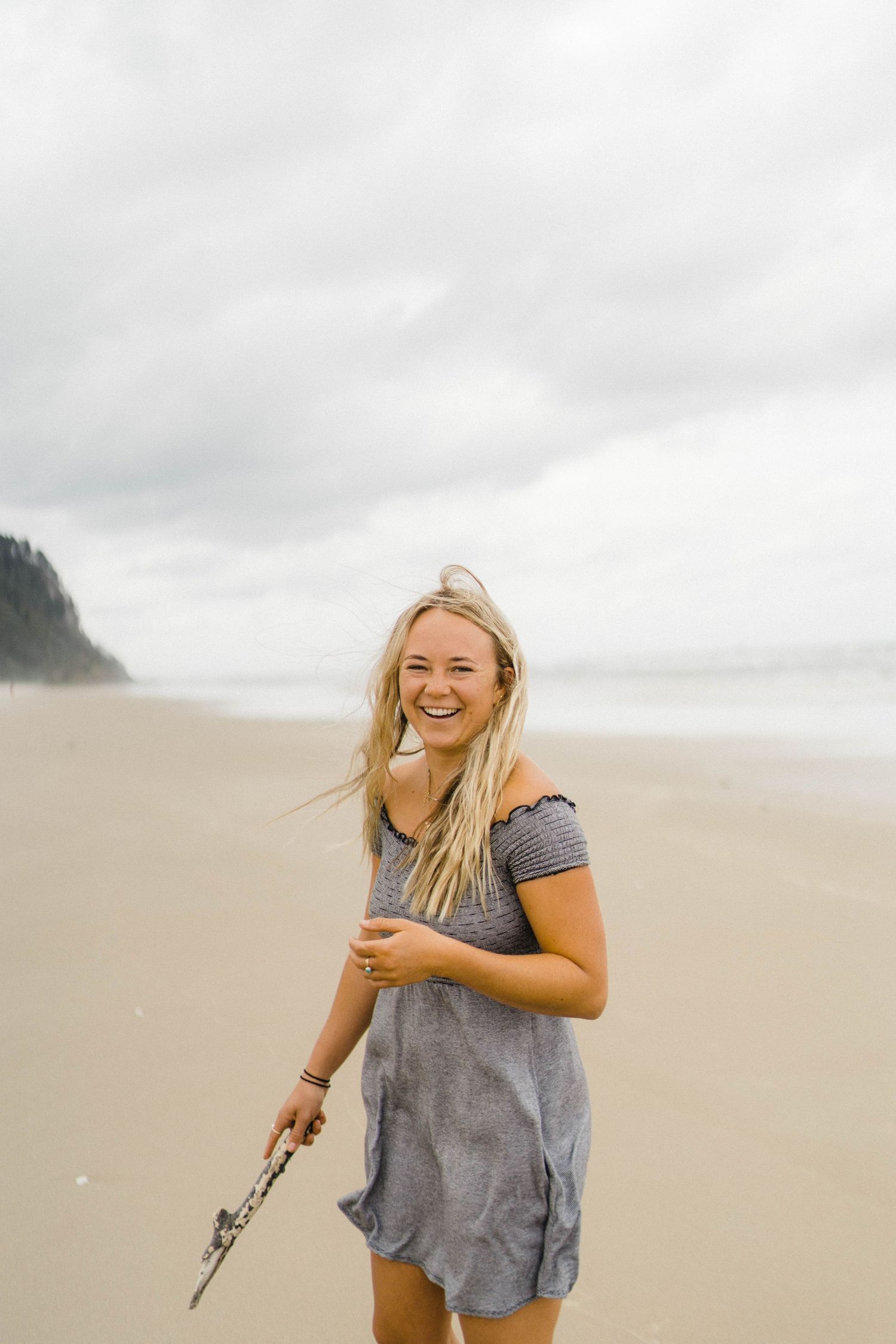 Person enjoying a carefree moment on cloudy beach with mountains in background.