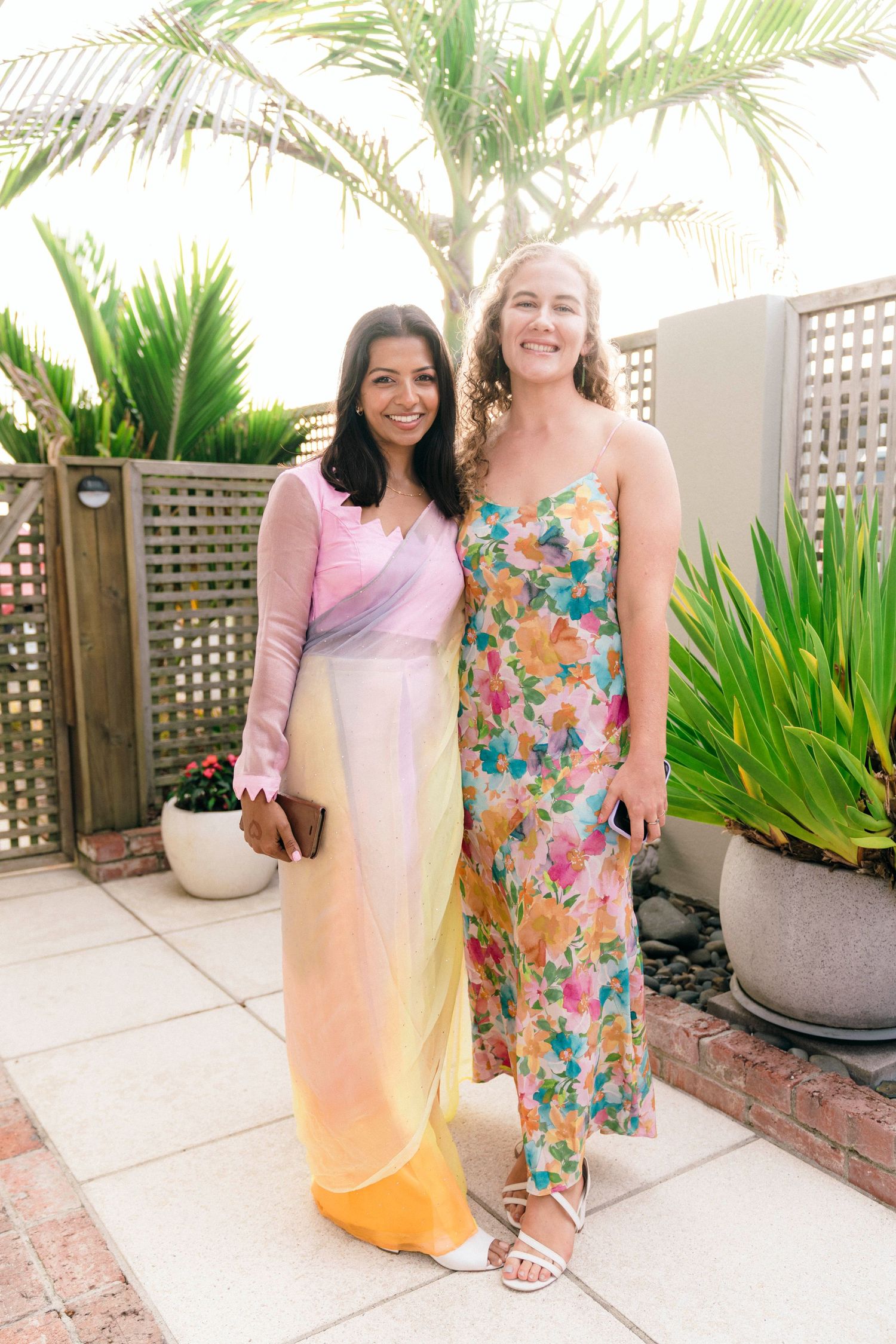 Two people posing together on a patio with tropical palm trees and privacy screens in background.