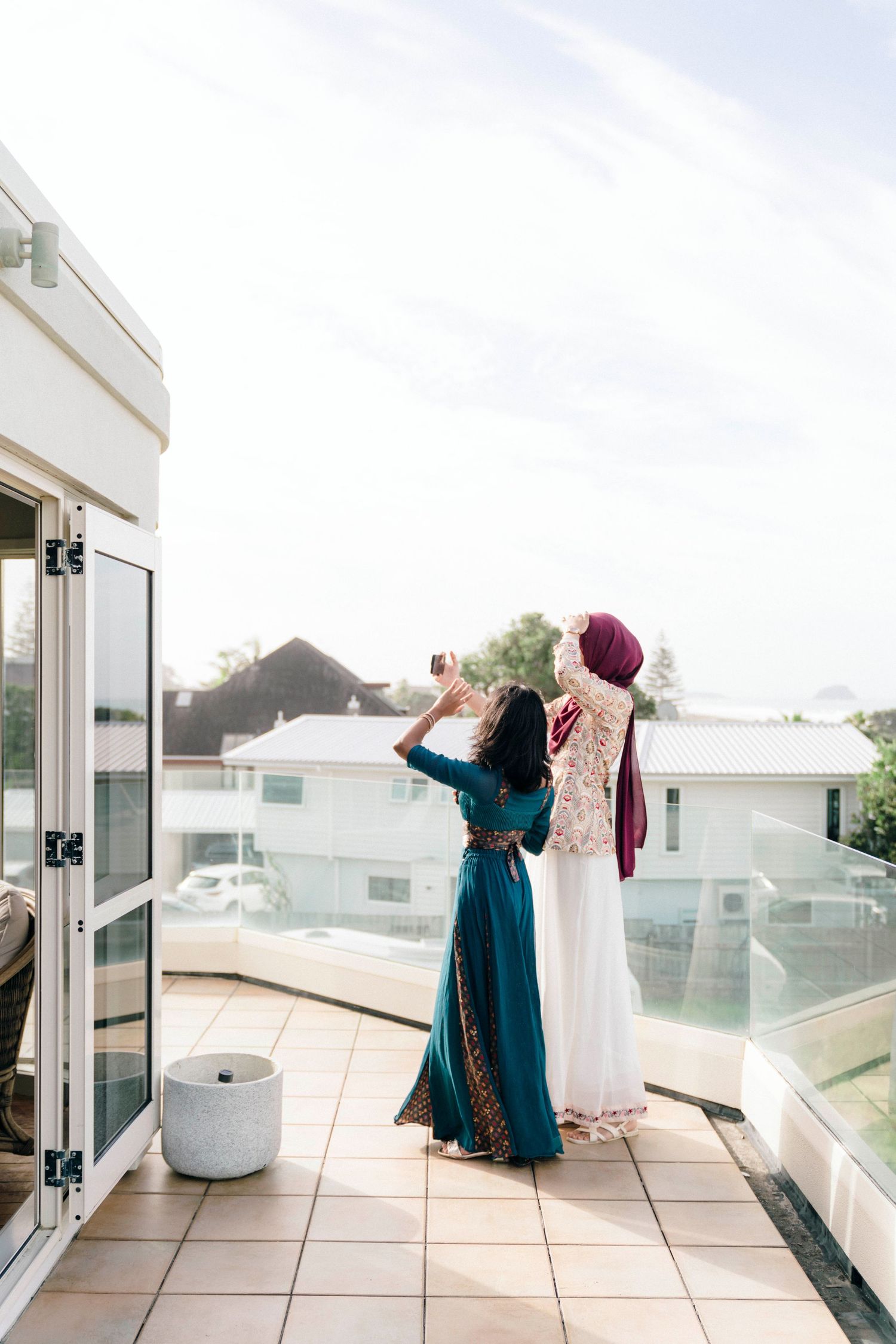 Two elegantly dressed guests in long gowns admiring view from rooftop terrace.