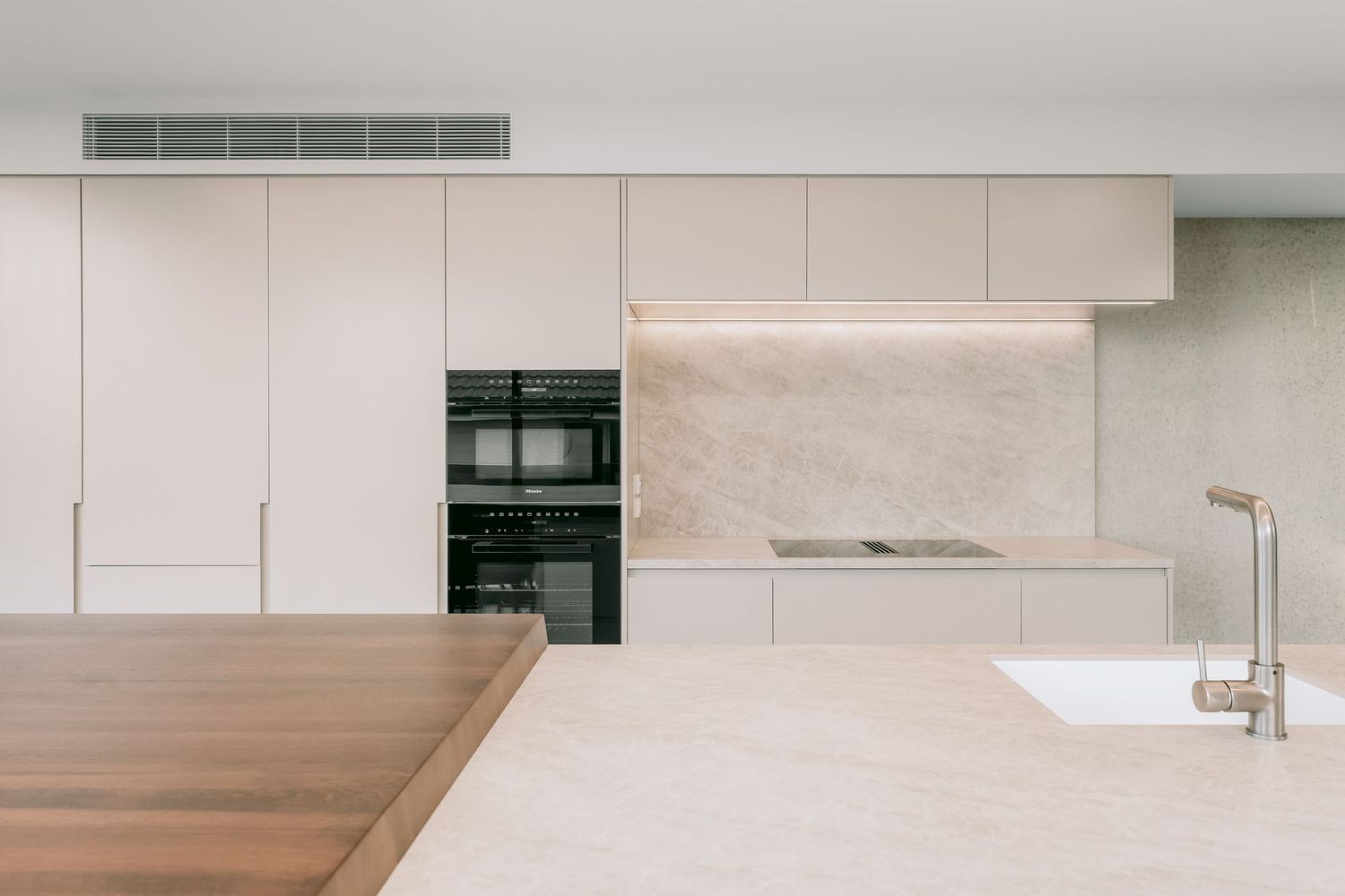 Sleek modern kitchen with integrated appliances and wooden countertop in neutral tones.