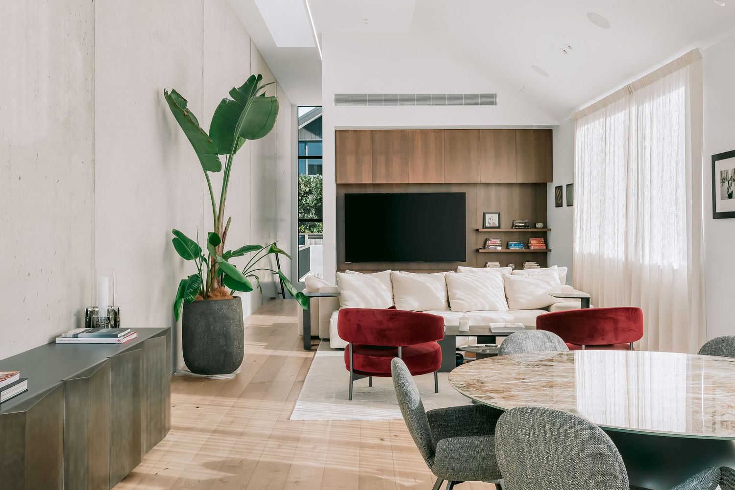 Modern living room with white walls, floating media cabinet, indoor plants, and stylish red accent chairs.