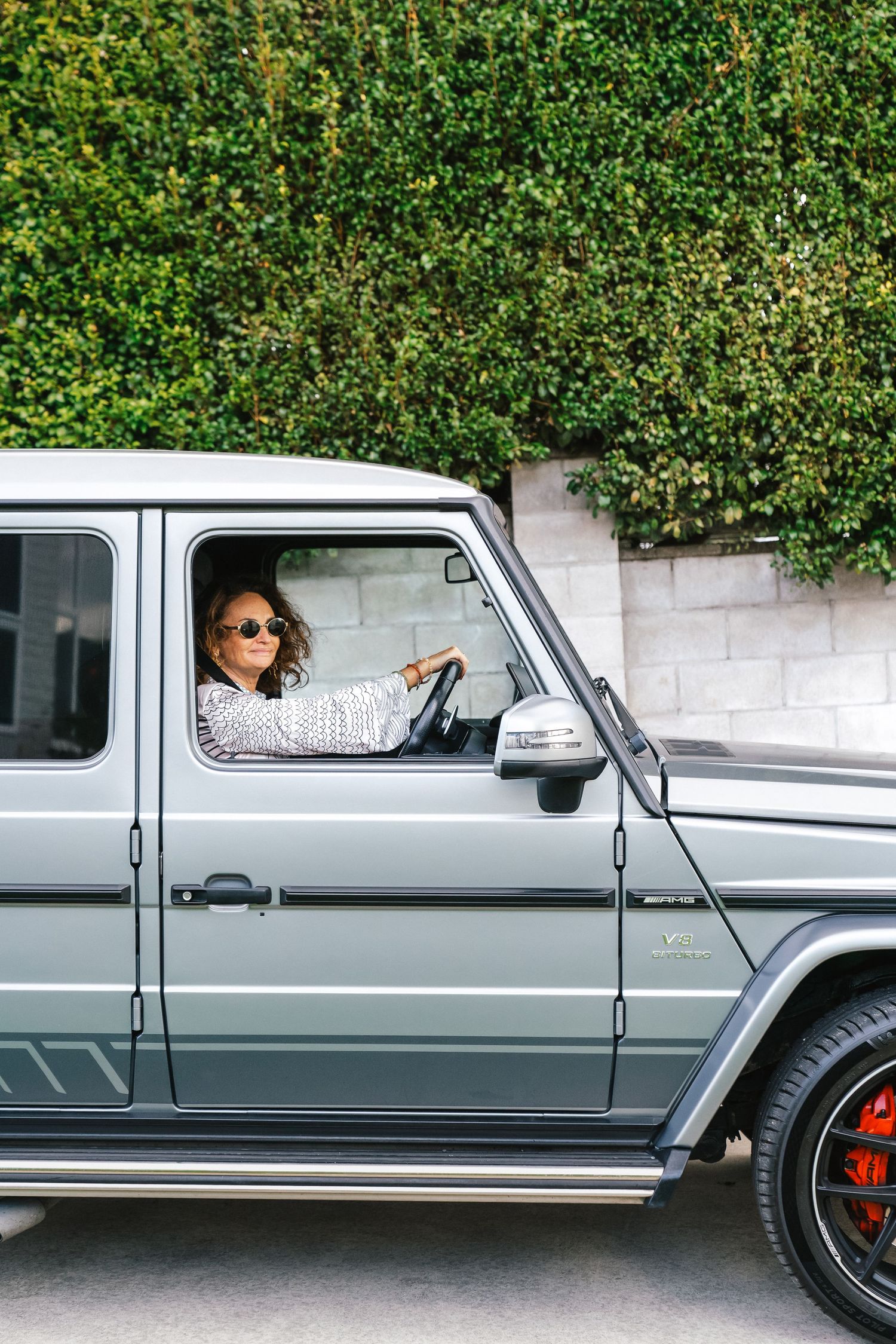 A classic silver Mercedes G-Wagon parked against a lush green hedge wall.