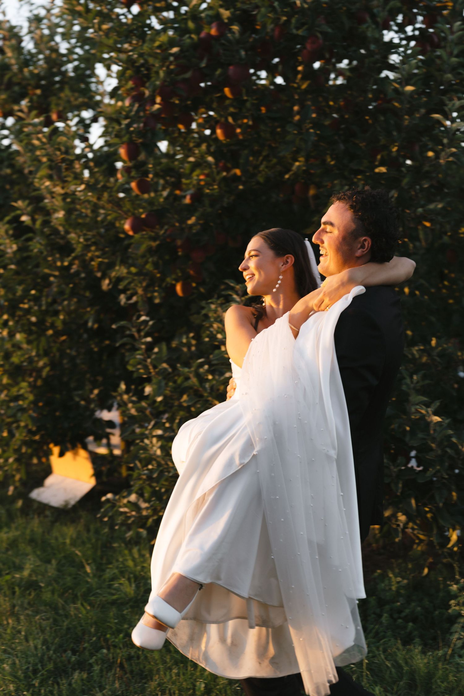 Newlyweds share joyful moments in a sunlit orchard during golden hour.