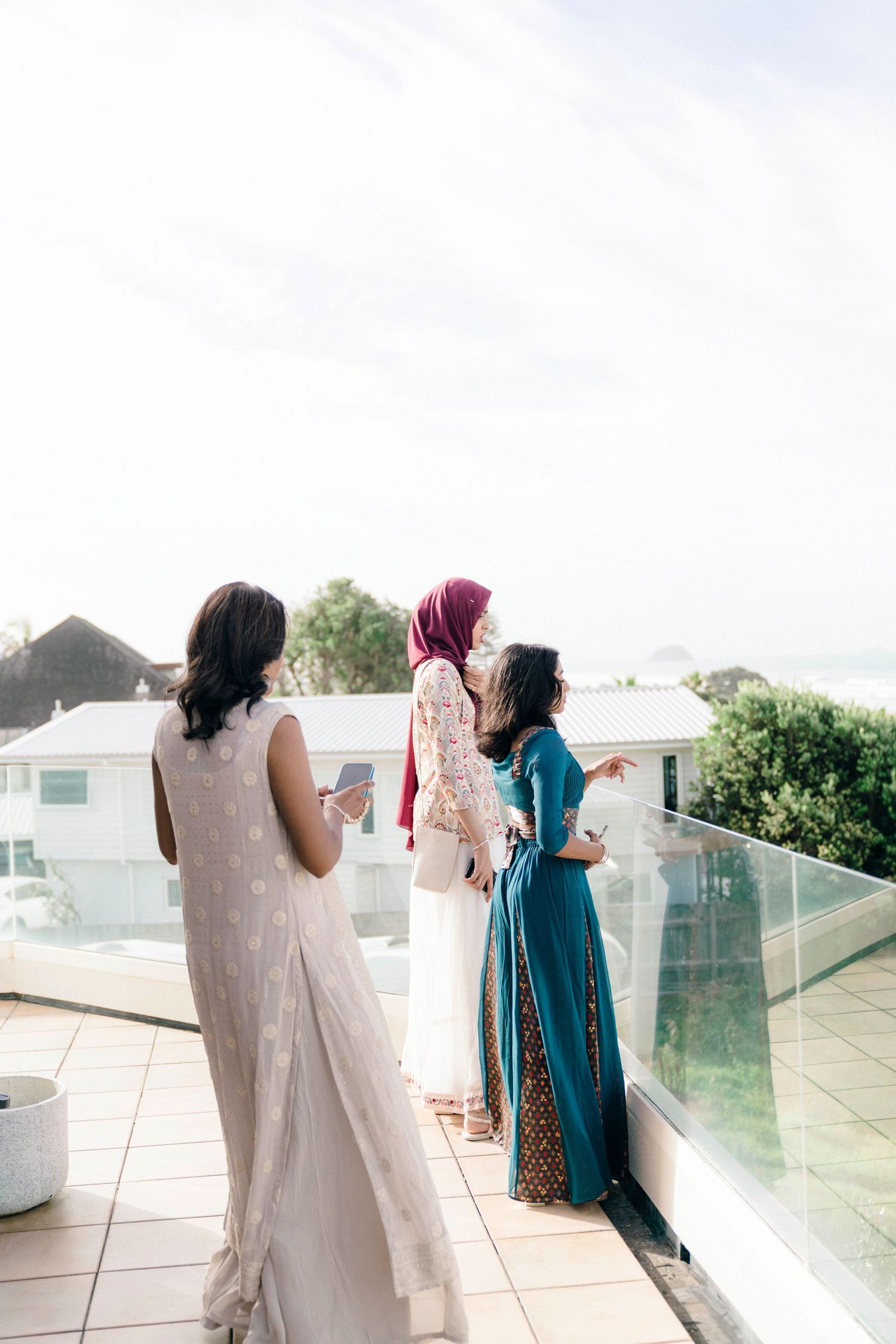 Three elegant guests admire the view from a balcony with glass railings.