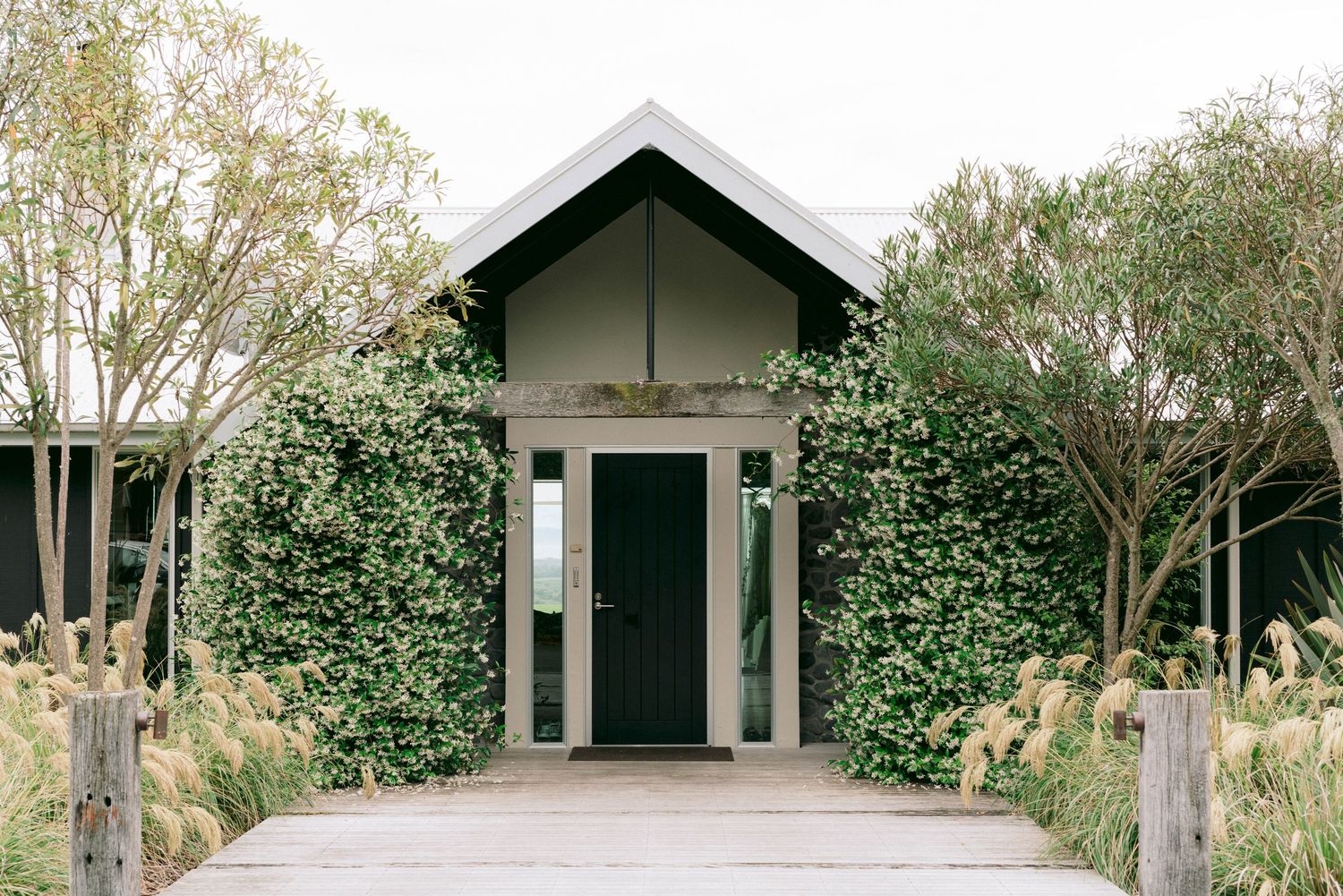 Row of rustic black and white cabins with peaked roofs surrounded by lush greenery.