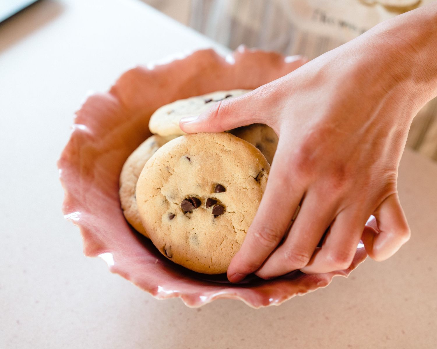 Hands shaping cookie dough into round shapes with chocolate chips on a baking surface.