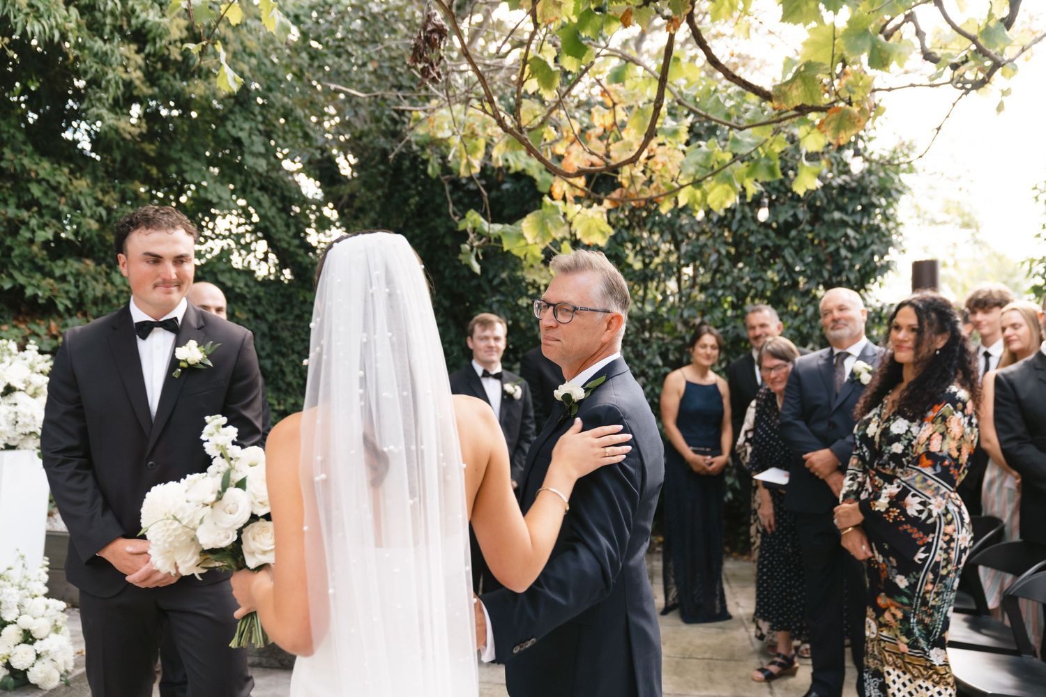 A bride and groom share their first dance surrounded by wedding guests during an outdoor reception celebration.