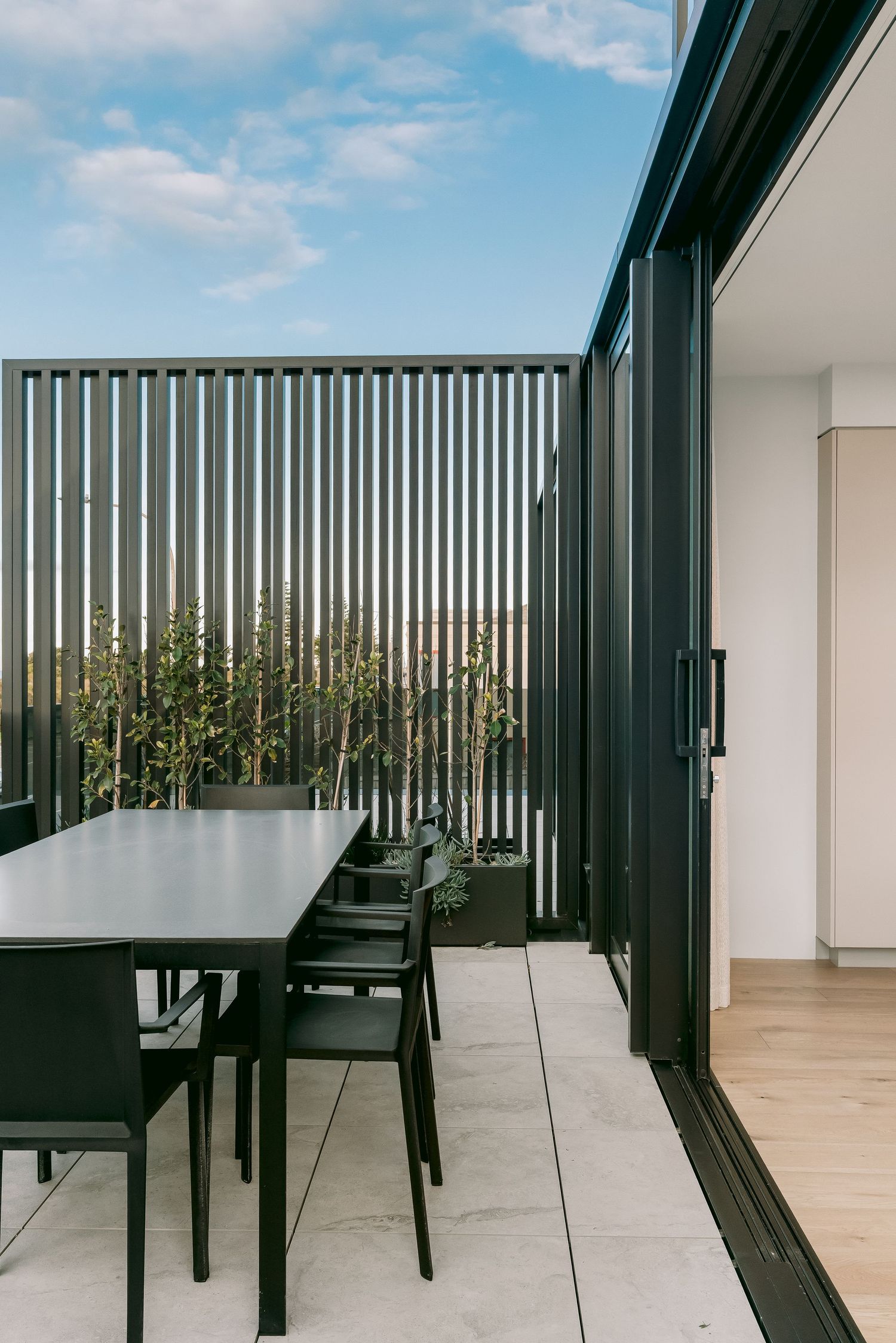 Contemporary balcony with black vertical slats and outdoor dining furniture against a blue sky.
