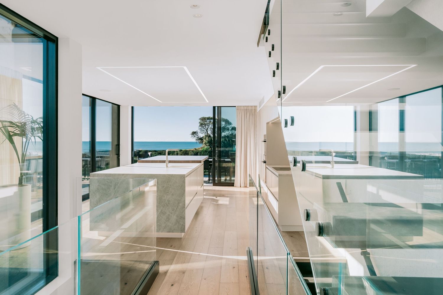 Interior of a luxurious beachfront property with floor-to-ceiling windows and white contemporary architecture.