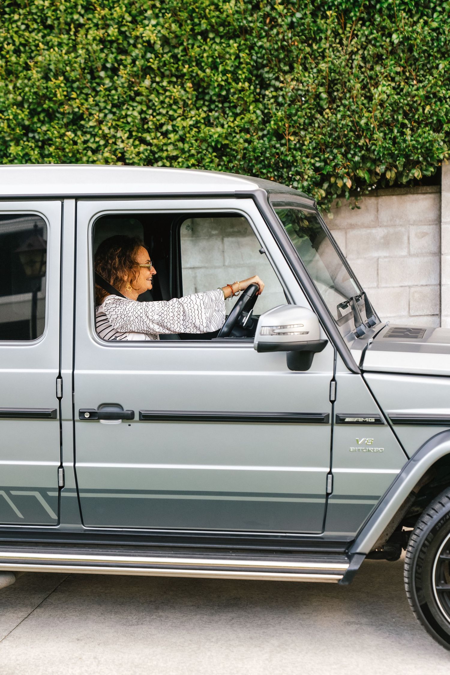 Side view of a silver Mercedes G-Class luxury SUV against a hedge backdrop.