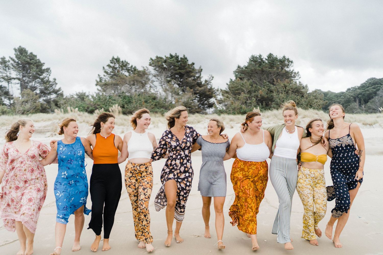 A group wearing colorful dresses and pants walks together along a misty beach shoreline.