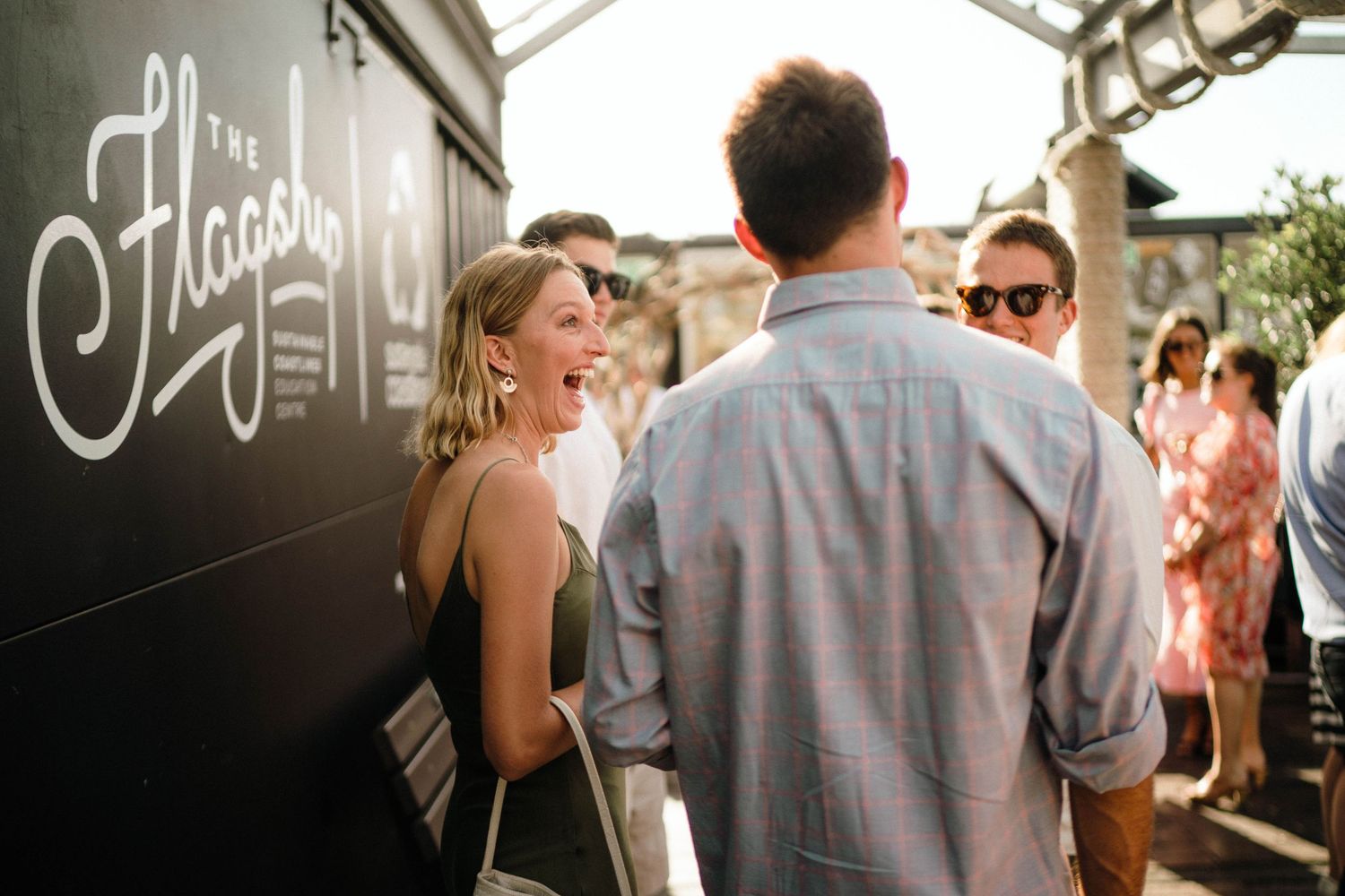 People gather and socialize near a food truck with script lettering signage during an outdoor event.