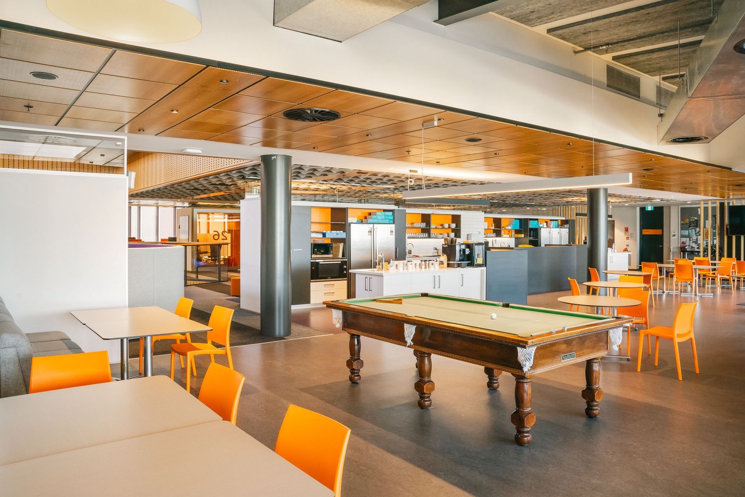 Modern office break room with pool table, orange chairs and wooden ceiling features in an open plan collaborative space.
