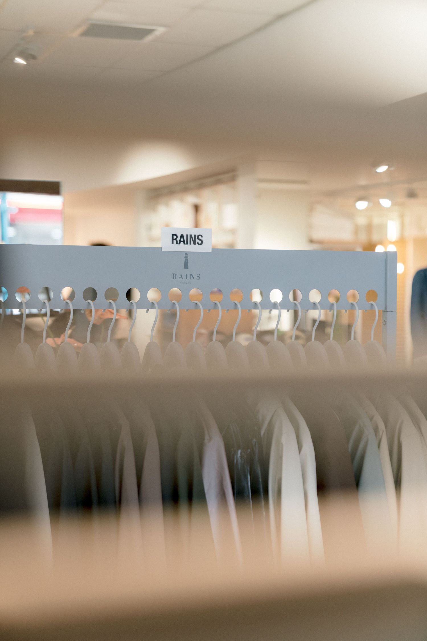 A row of empty wall-mounted coat hooks in an office hallway appears as a blurred silhouette pattern against a white wall.
