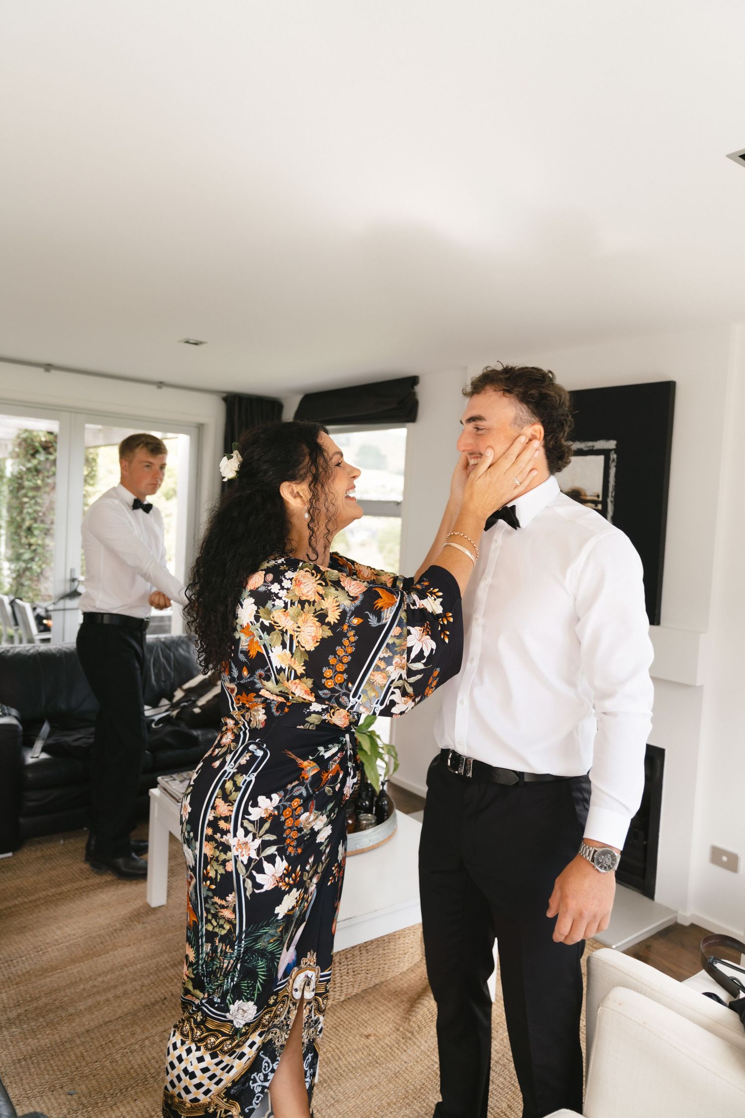 Wedding party members in floral dress and formal wear interact in a bright modern room.