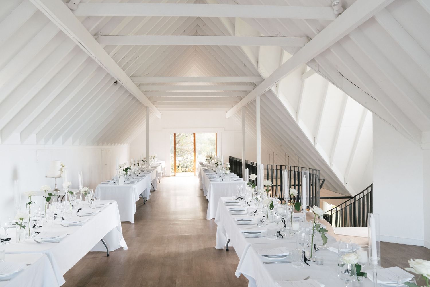 Clean white reception venue with vaulted ceiling and minimalist table settings.