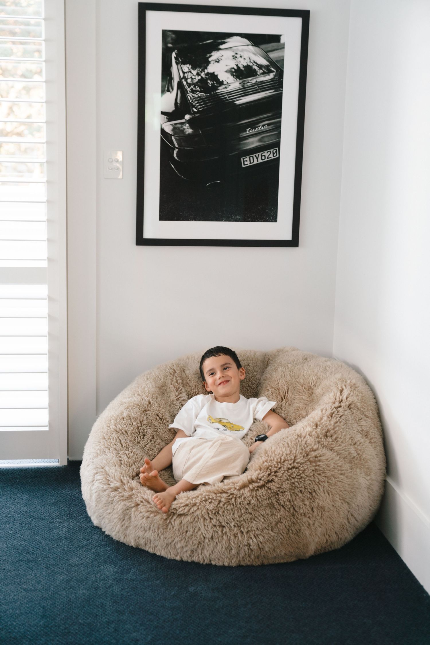 Child relaxing on a plush beanbag chair beneath black and white framed wall art.