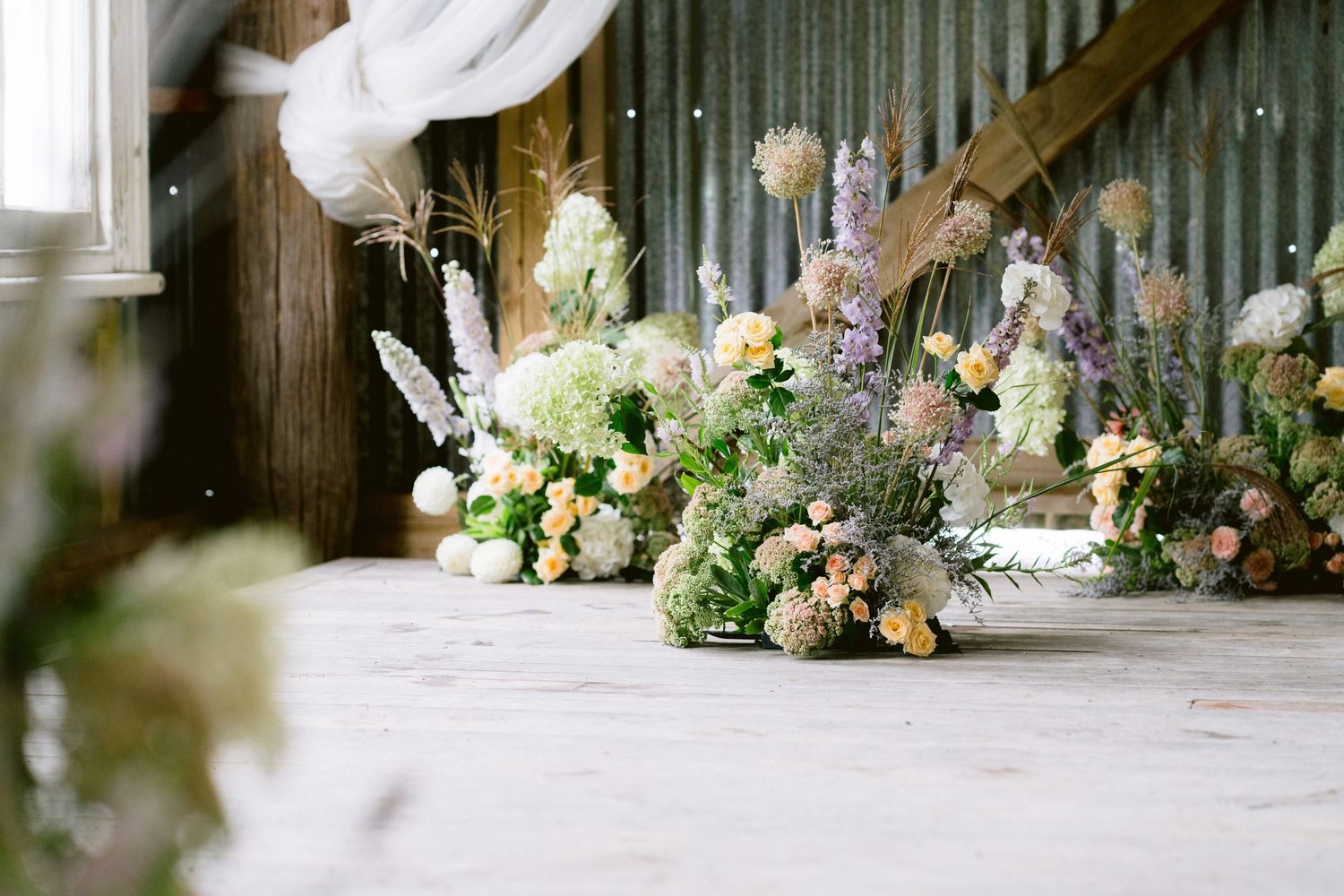 Wedding reception decor featuring soft floral arrangements and white draping in a rustic barn setting.