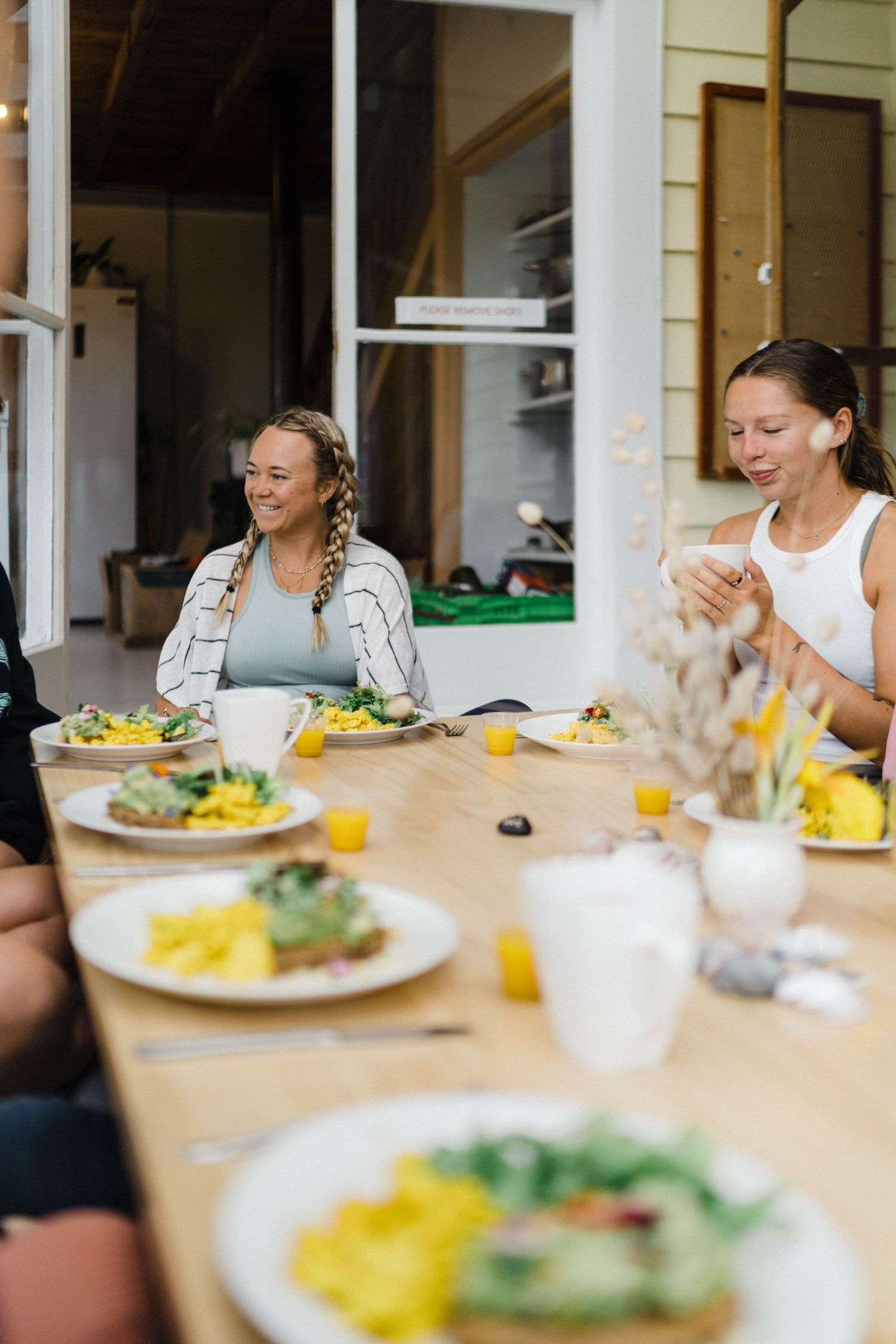 A group of people gathered around a dining table sharing a casual meal with plates of food and orange juice.