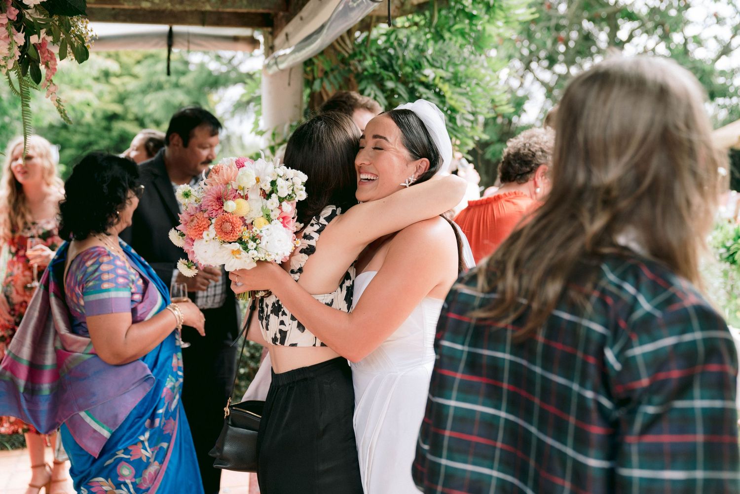 A joyful celebration with people hugging and embracing under a covered outdoor area with floral decorations.