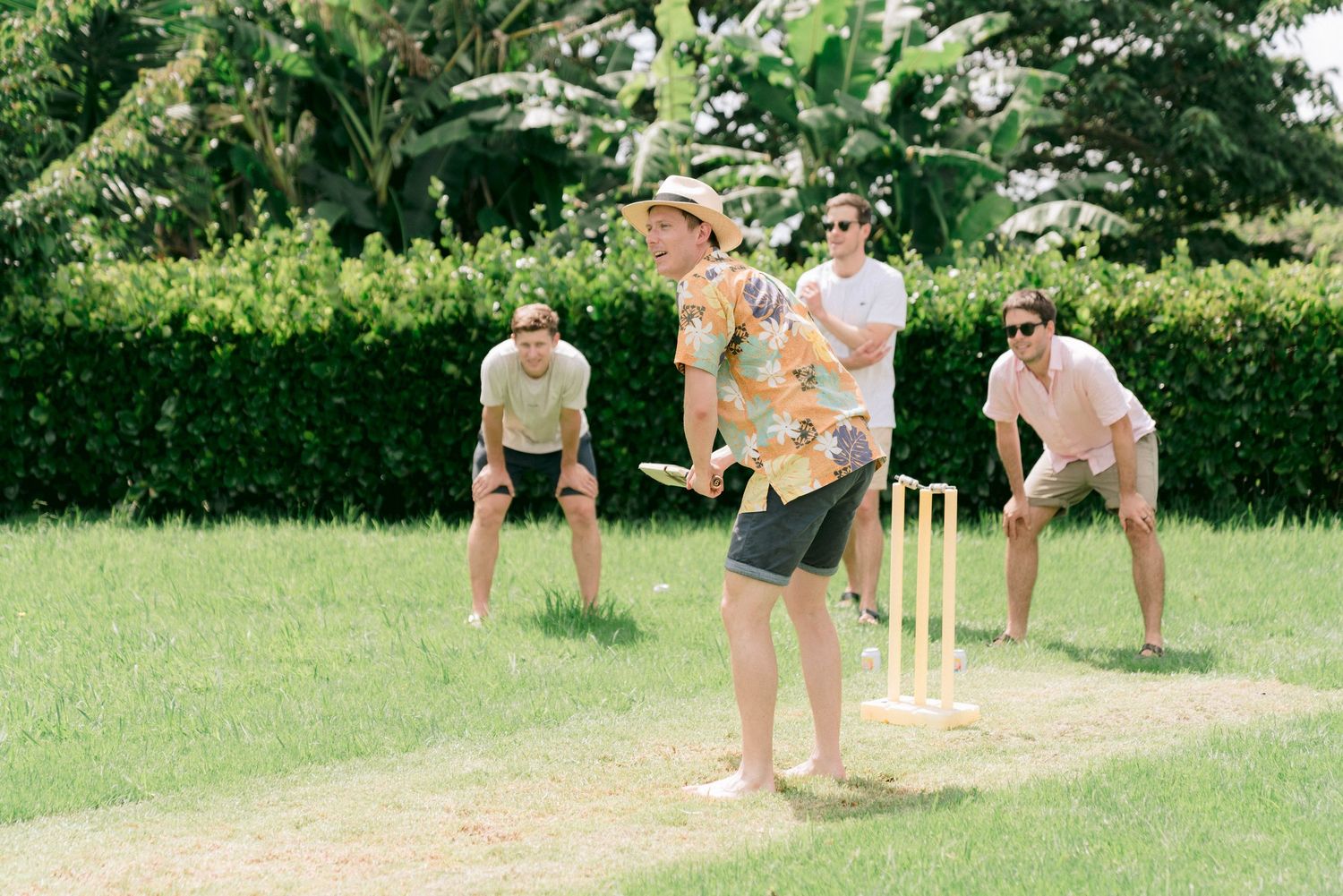Group playing cricket on a sunny green lawn during outdoor wedding festivities.