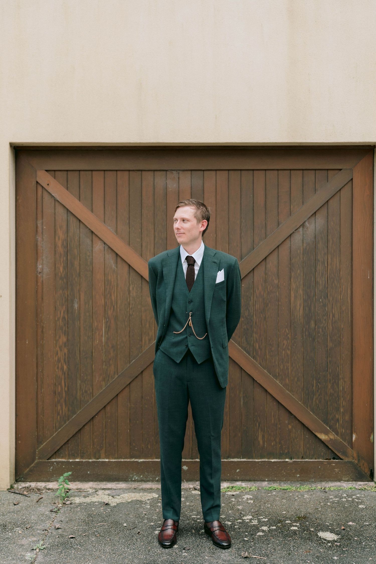 Formal portrait against wooden barn doors showing green suit and dress shoes.