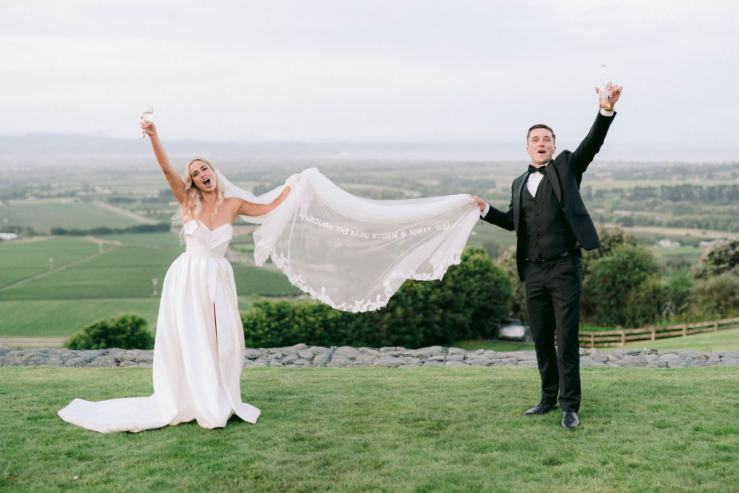Joyful celebration on a hilltop overlooking a scenic valley with flowing wedding veil.