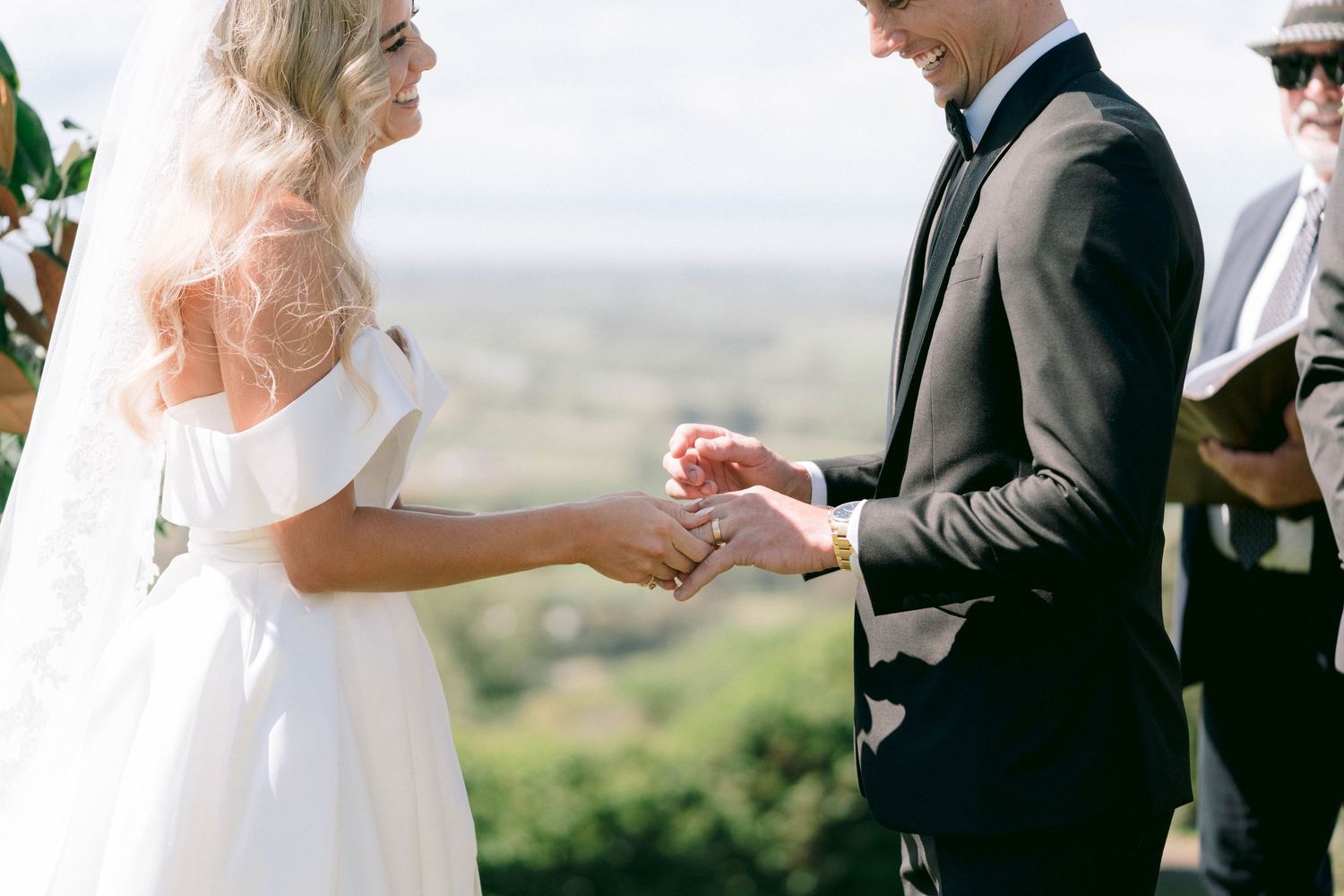 Close-up of wedding ring exchange ceremony with scenic countryside backdrop.
