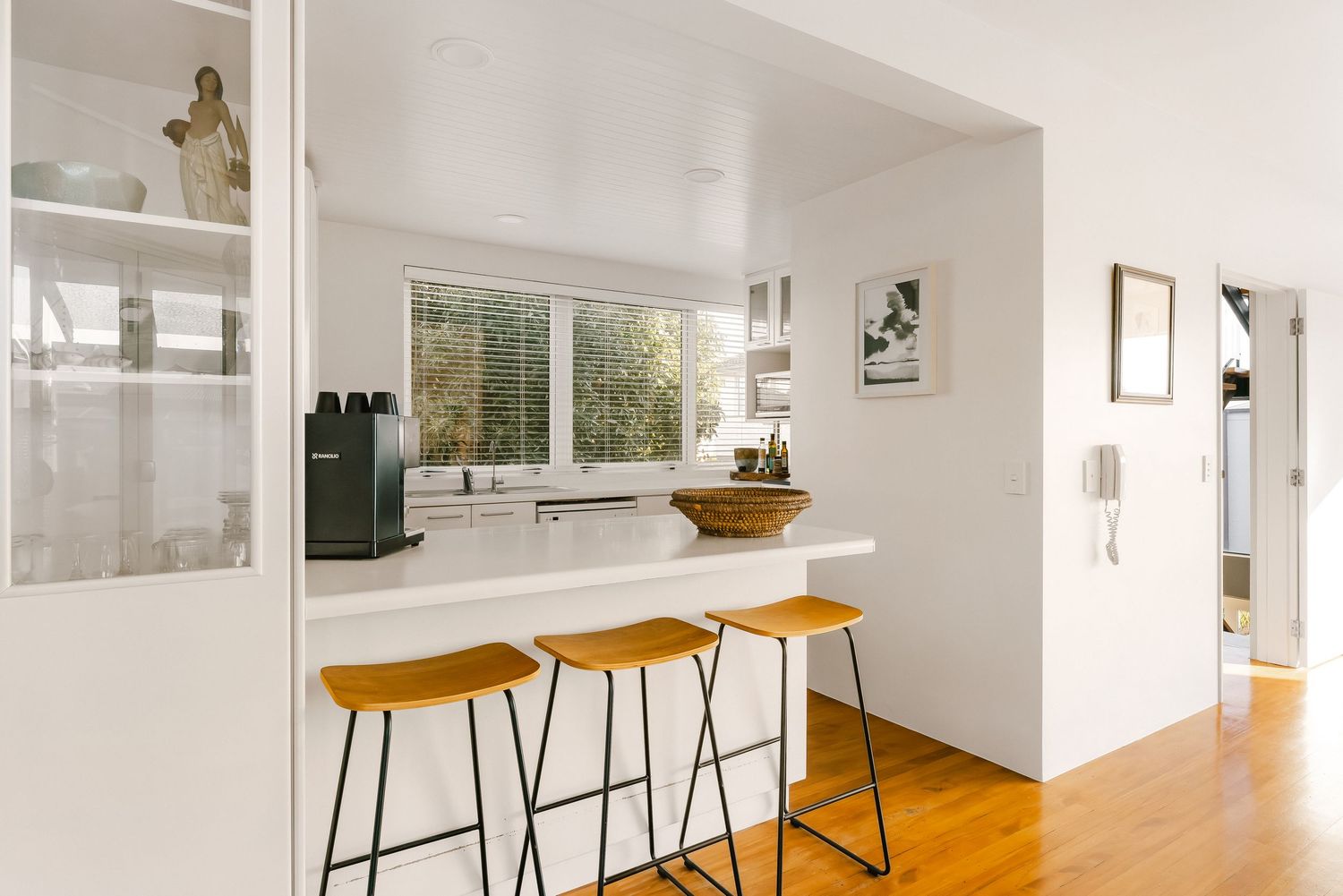 Modern kitchen bar area with wooden stools and bright window view.