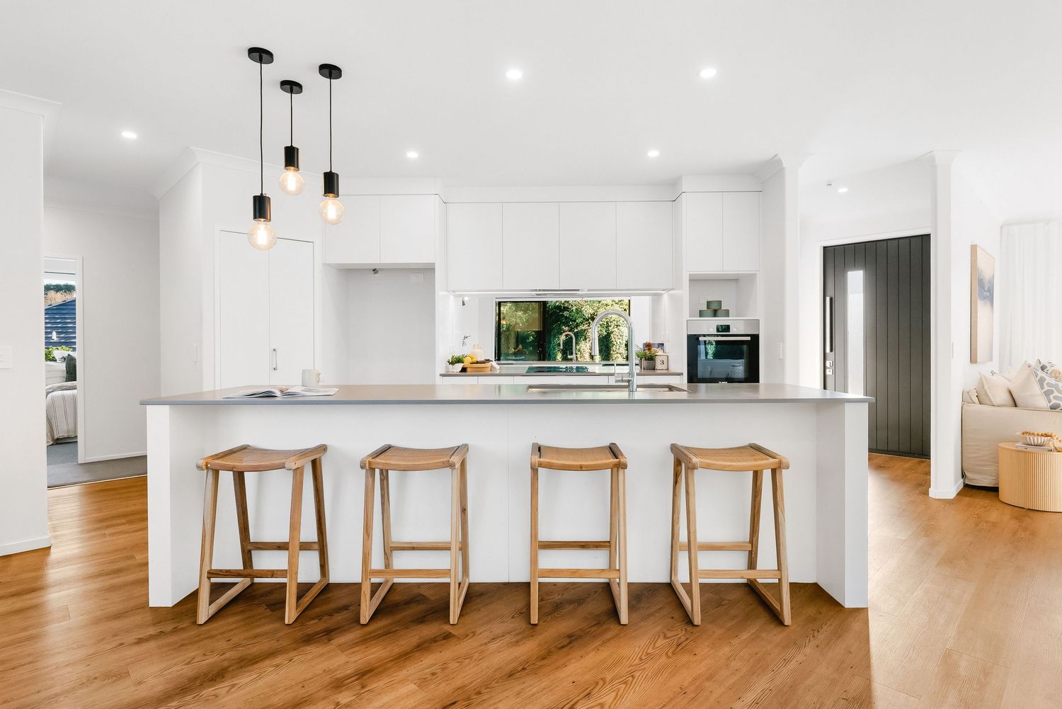 Modern white kitchen panorama with wooden counter stools and pendant lights in a bright open concept space.