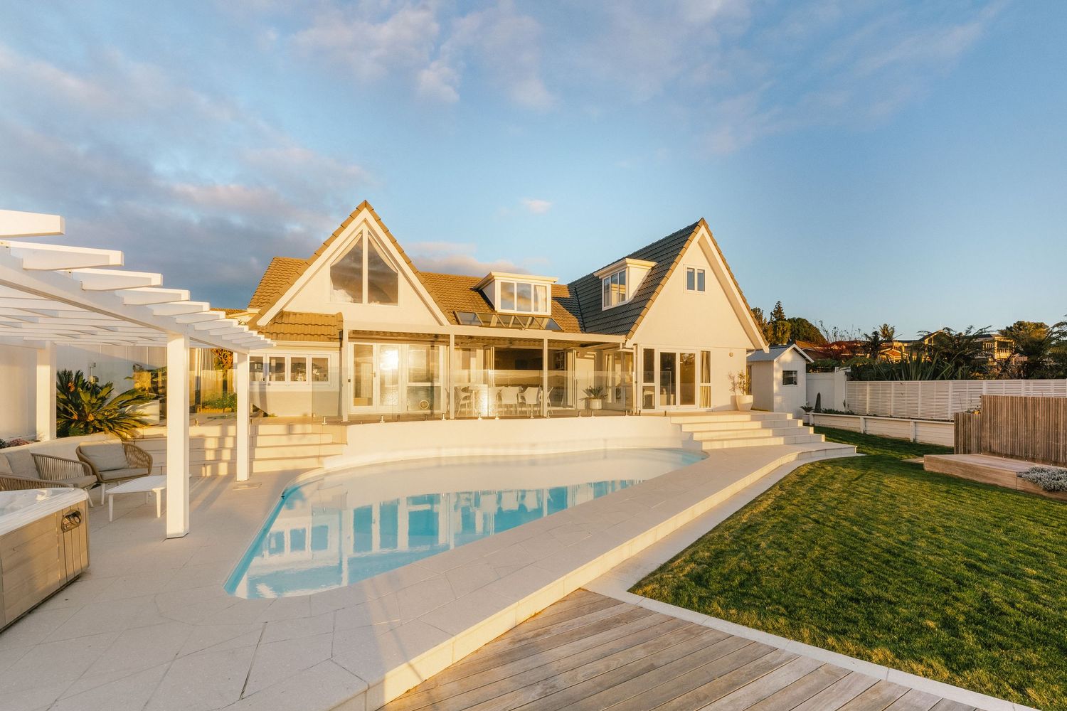 Expansive oceanfront property with infinity pool and landscaped lawn during golden hour.