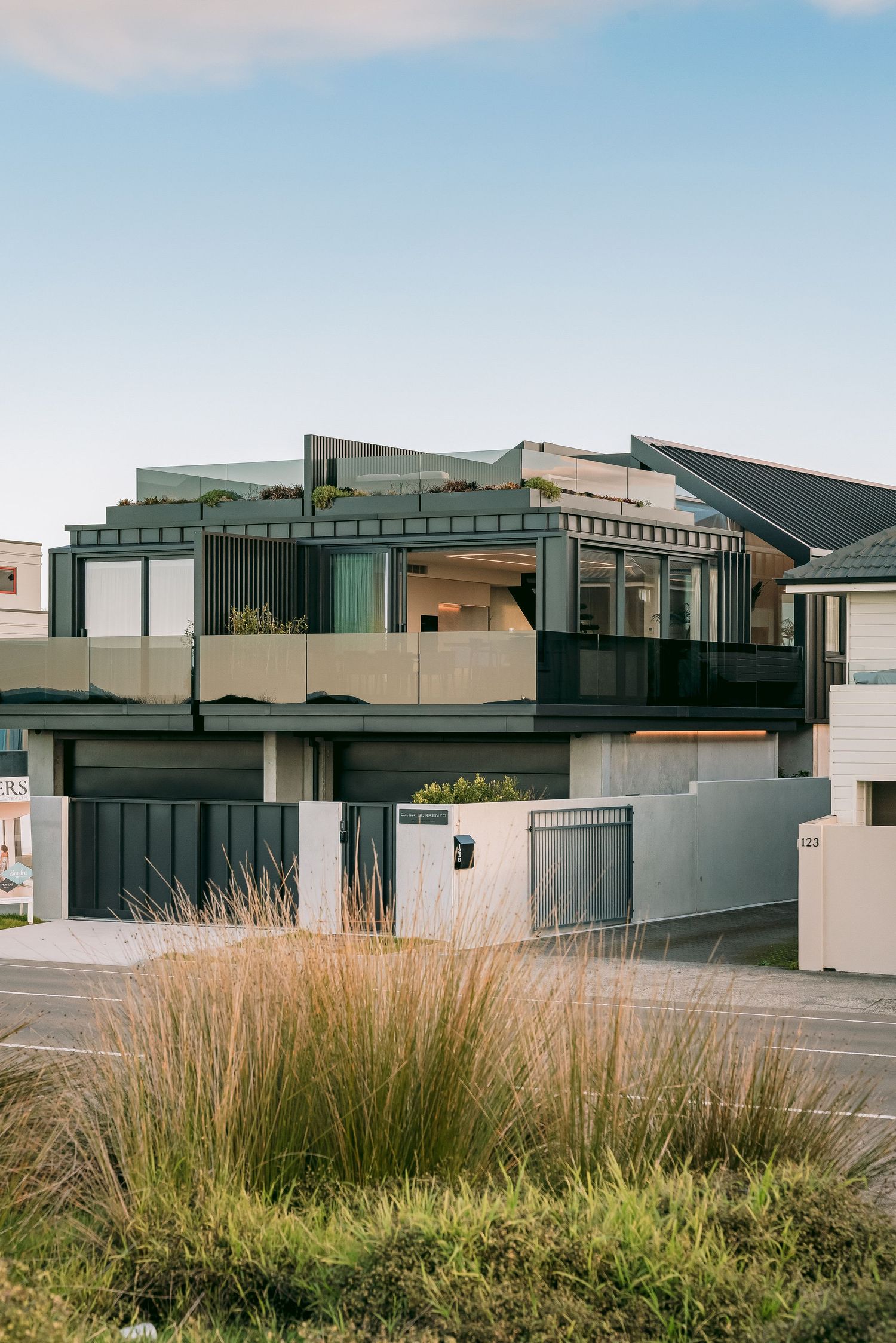 Modern two-story luxury home with angular architecture and glass panels set against a blue sky.