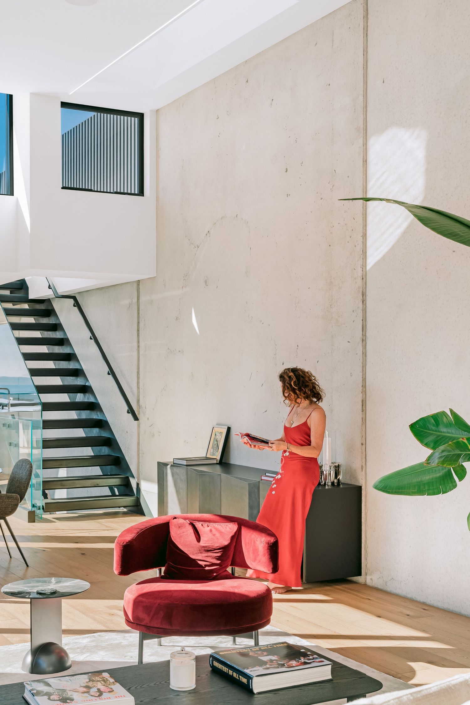 Modern minimalist living room interior with red accent chair and black stairs leading upward.