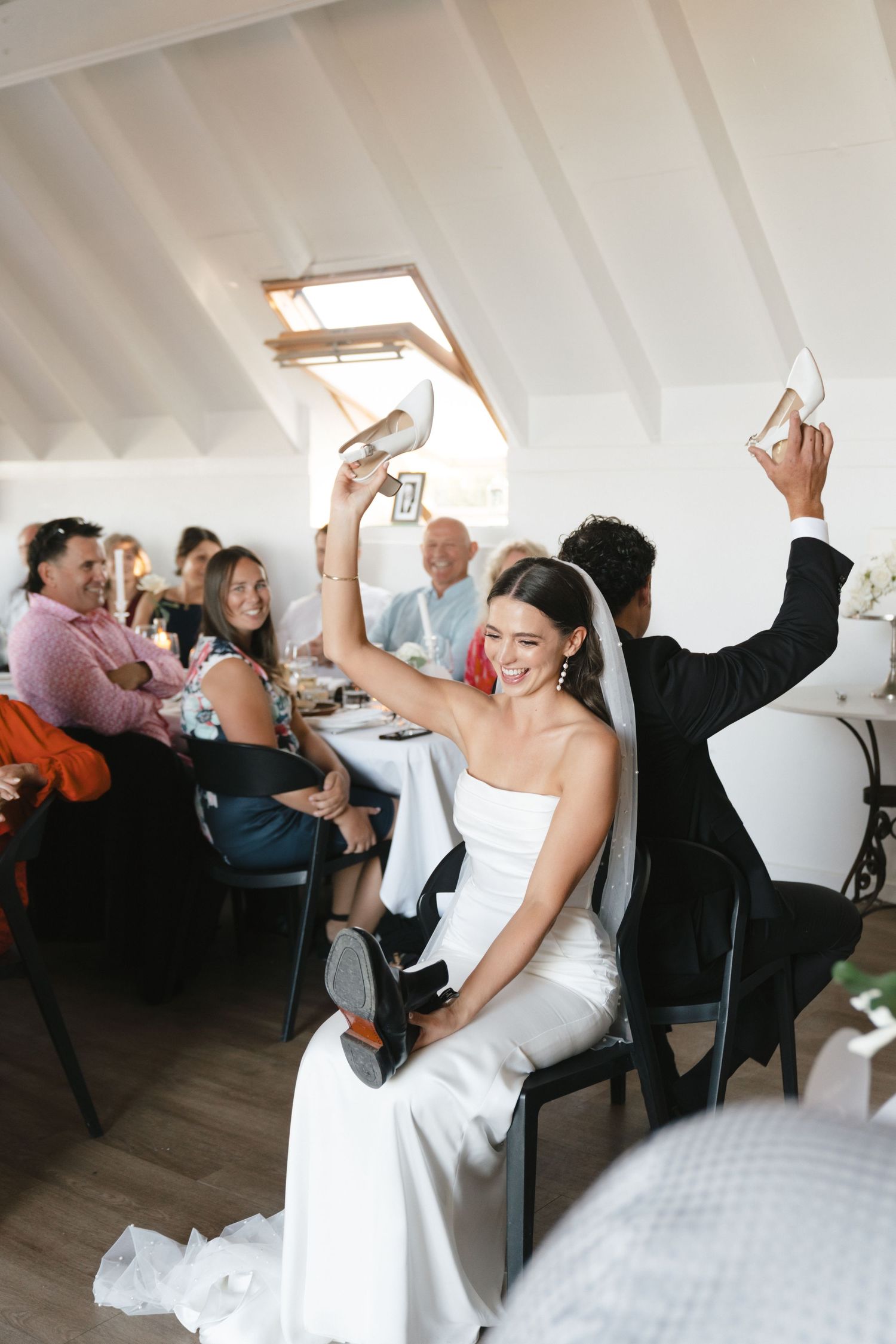Newlyweds and wedding guests raise champagne glasses in celebration at an intimate reception in a bright venue.