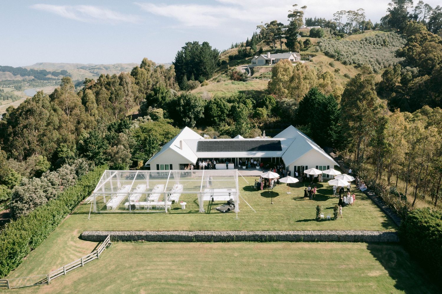Aerial view of an elegant outdoor wedding venue with white tent and mountain backdrop.
