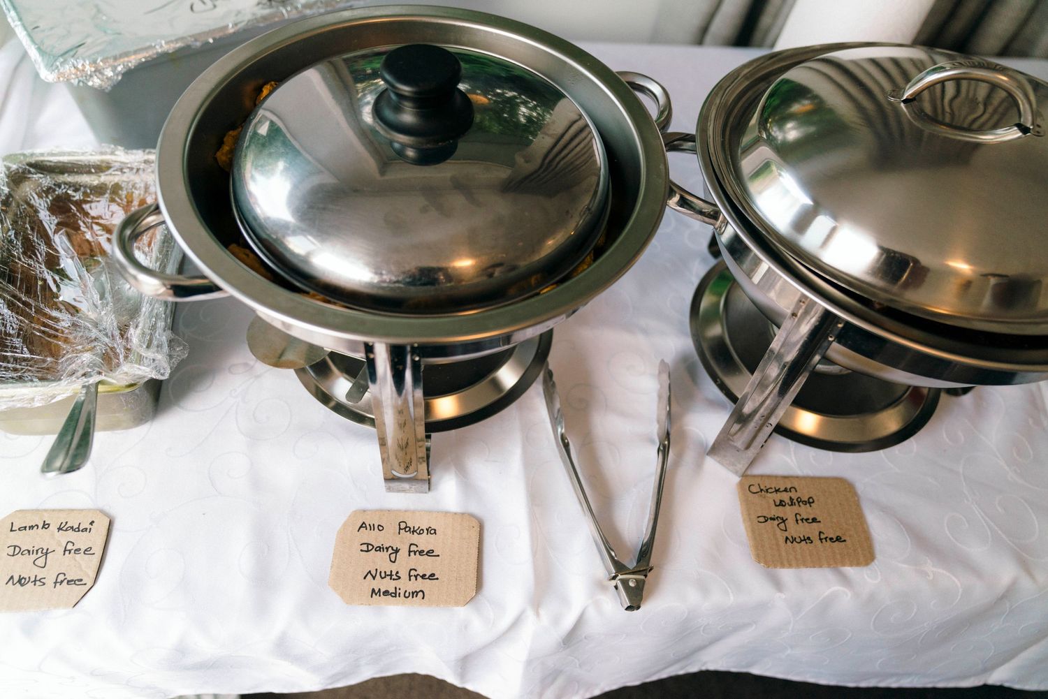 Row of silver chafing dishes and serving stations at a buffet setup.