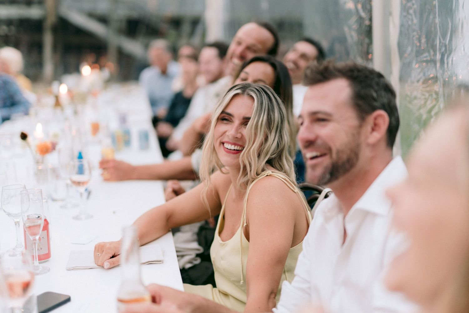 Wedding guests smile and celebrate during an outdoor reception dinner.