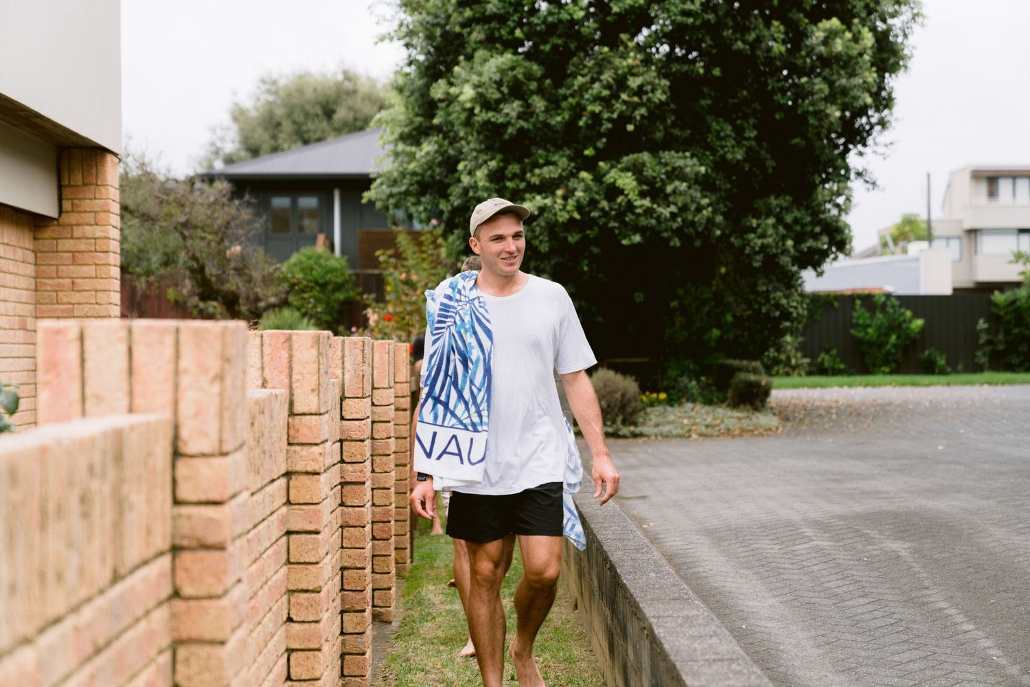 Person walking down pathway next to brick wall and trees on sunny day.