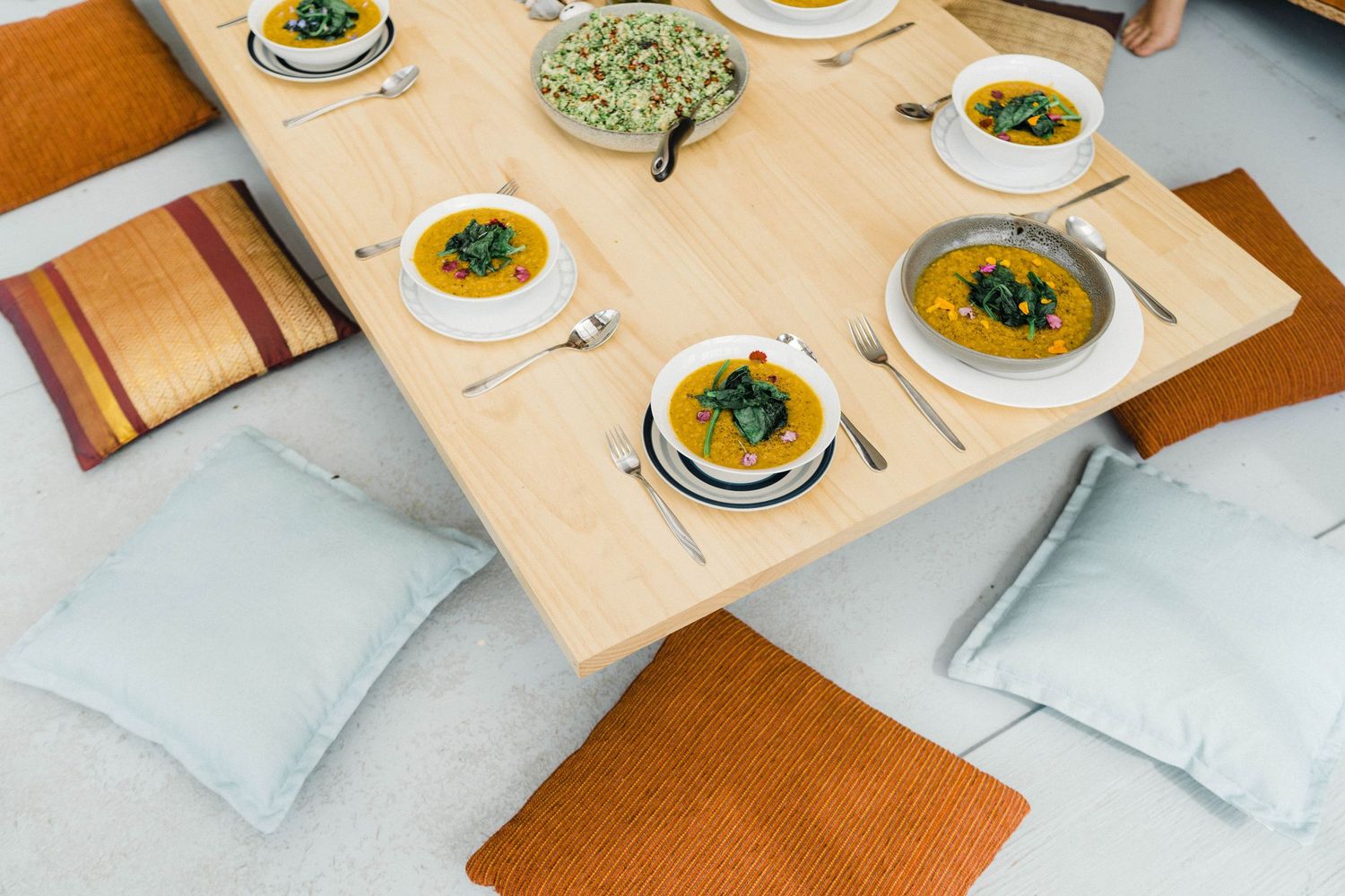 Modern table setting with orange cushions and white bowls of soup arranged symmetrically.
