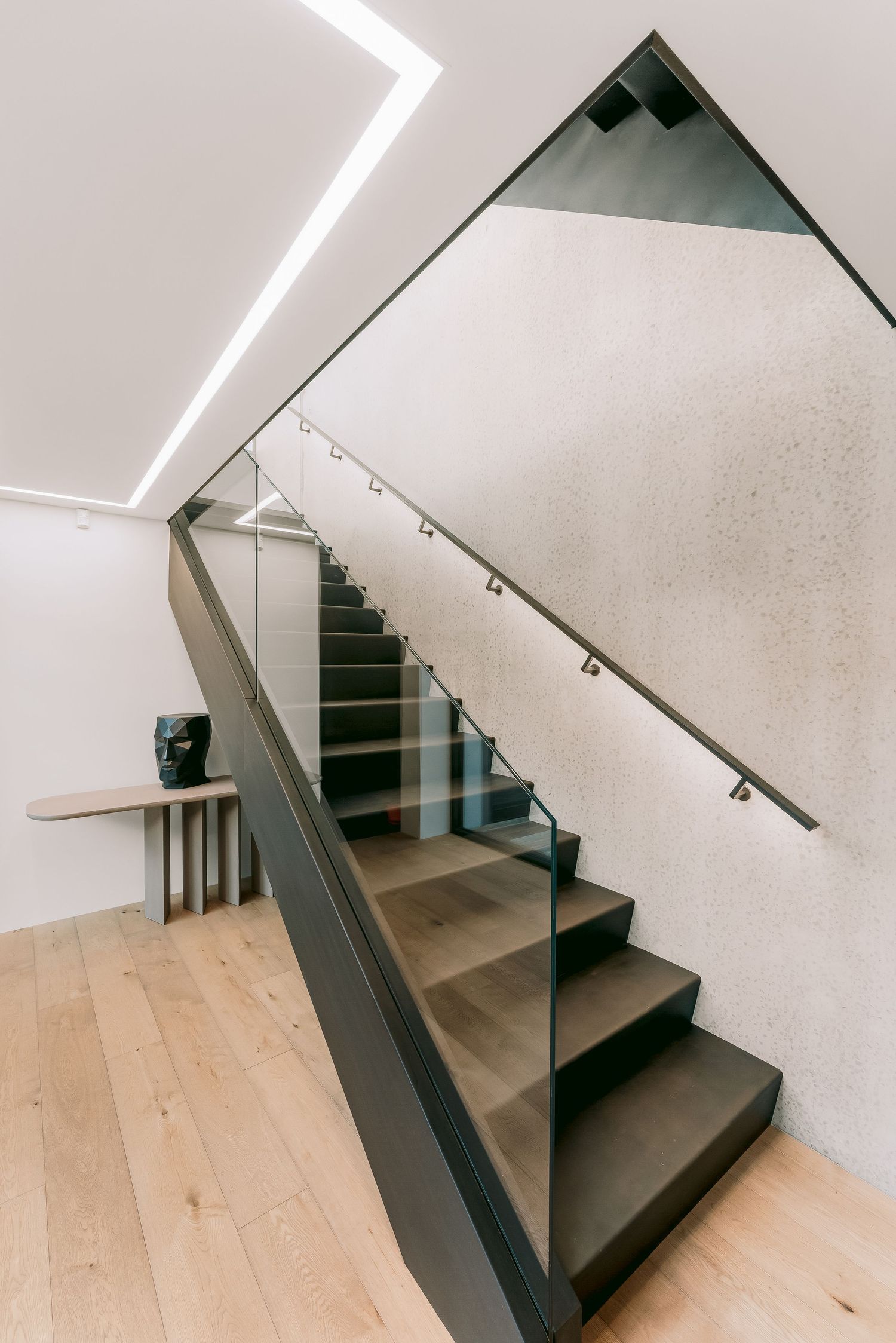 Modern interior staircase with black steps, glass railing, and LED lighting along white walls.