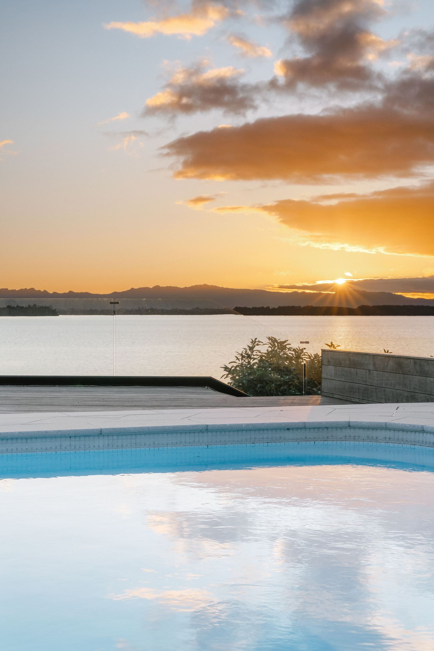 Tranquil infinity pool reflecting orange sunset sky over calm waters.